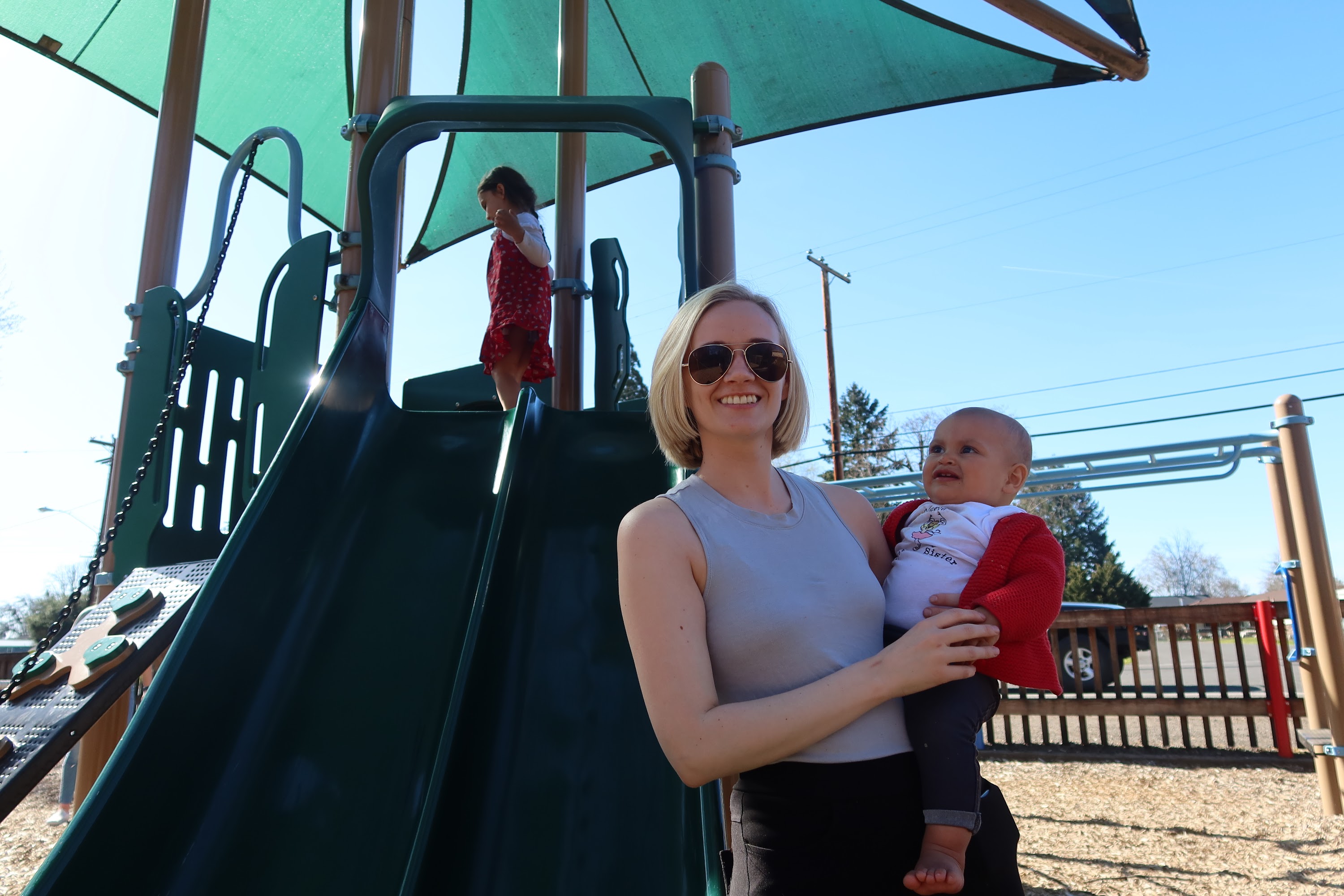 Mother Holding Baby at Playground with Child on Slide