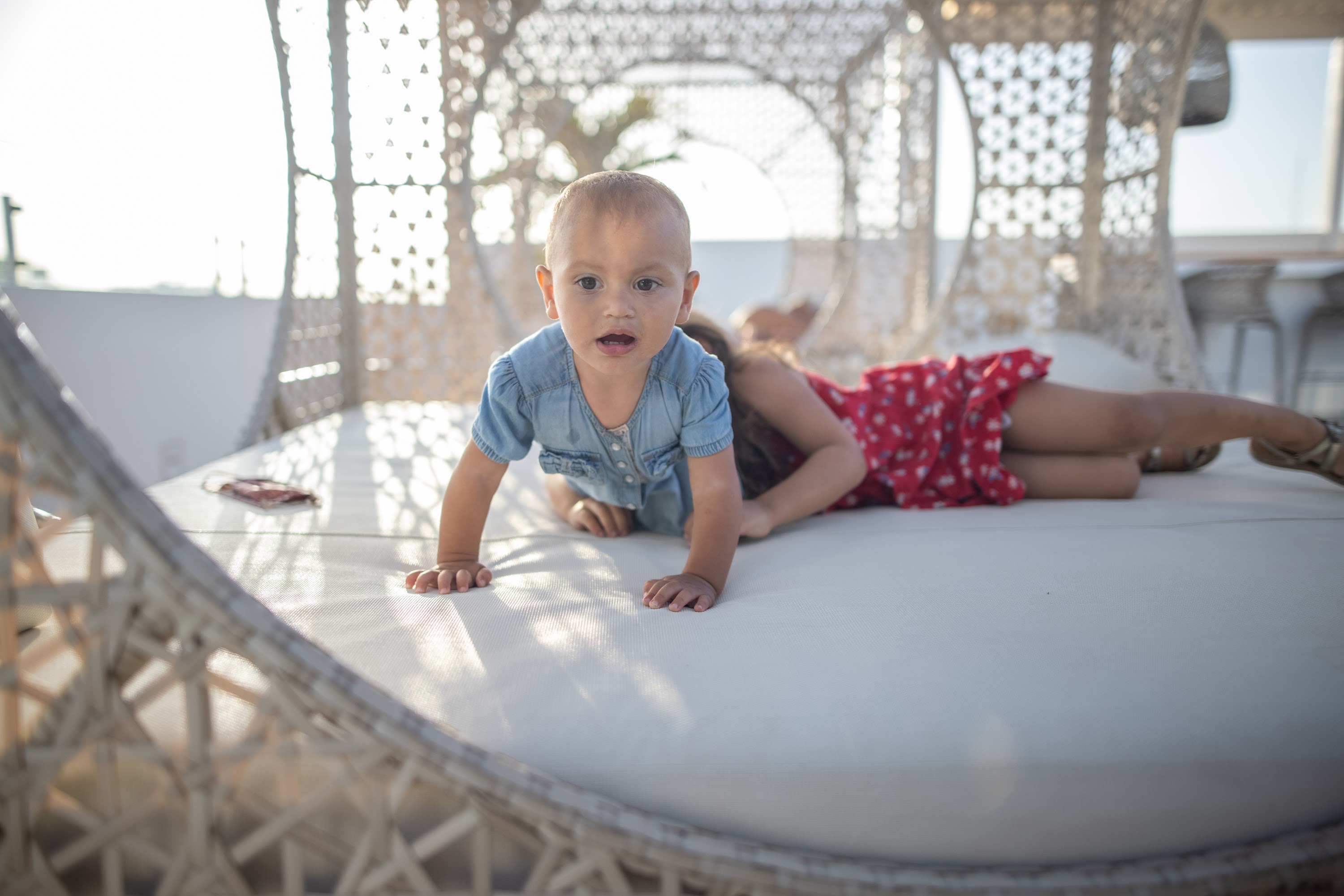 Baby Crawling on Rooftop Daybed with Woman in Background