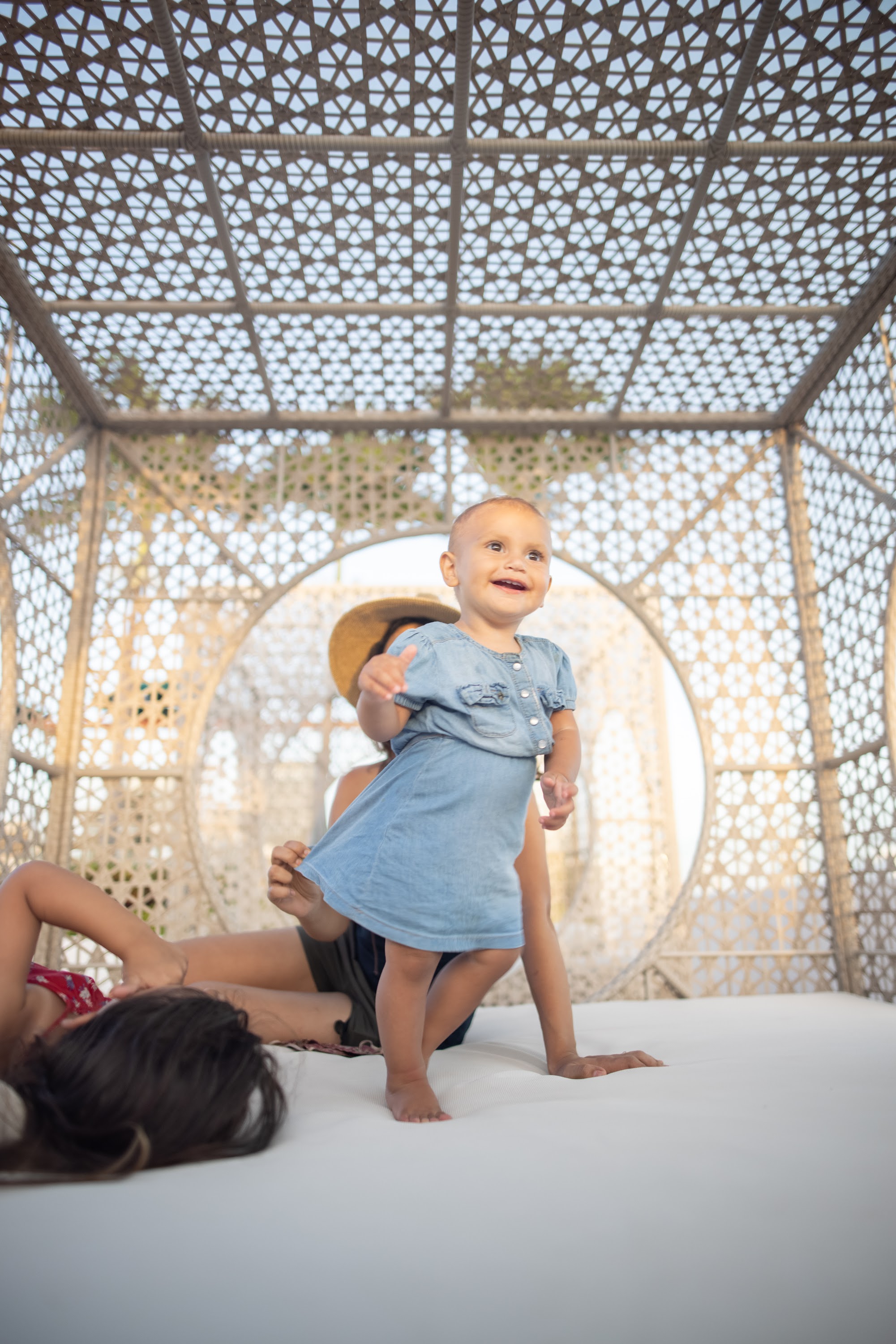 Baby in denim dress smiling under a lattice canopy