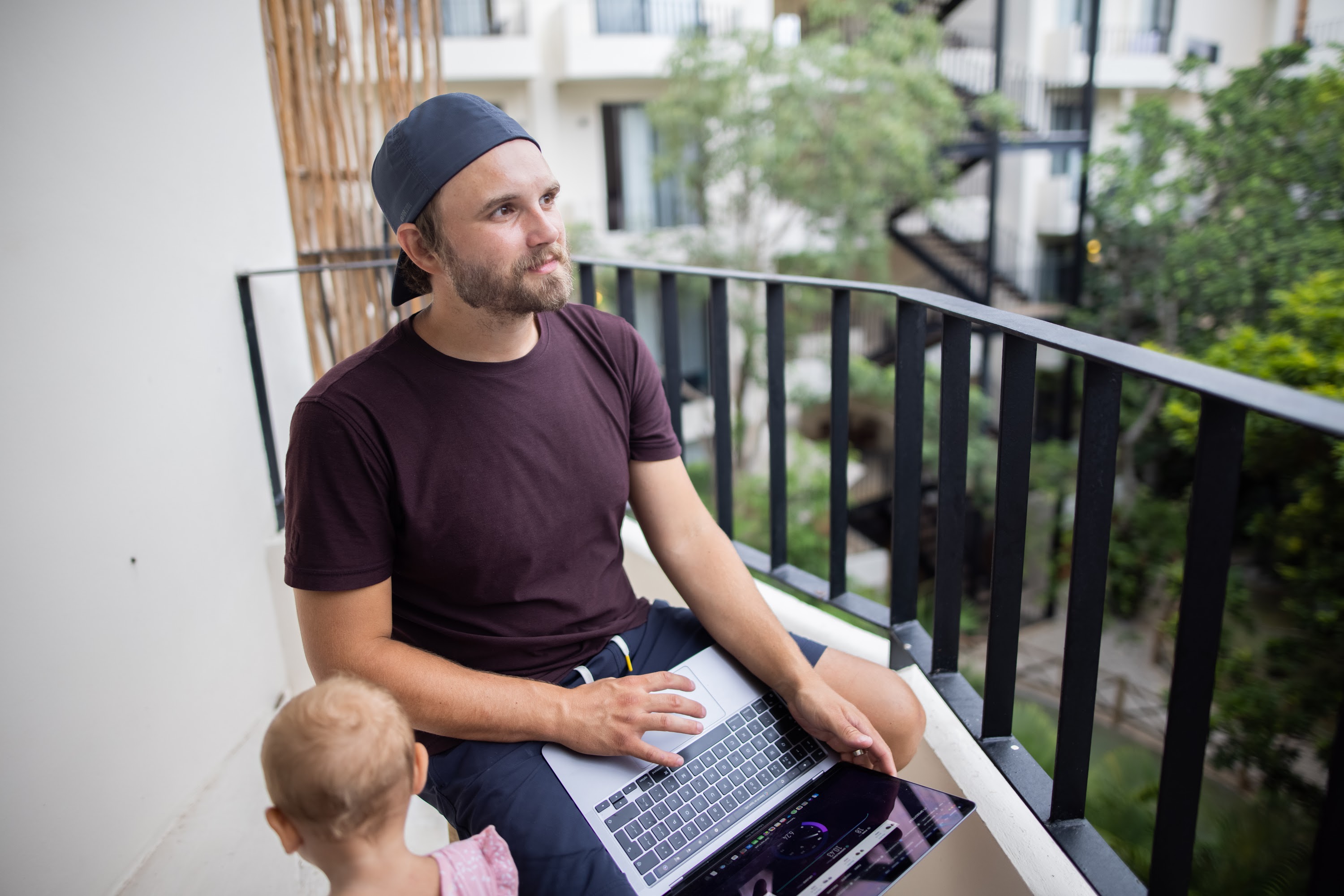 Man Working on Laptop on Balcony with Child