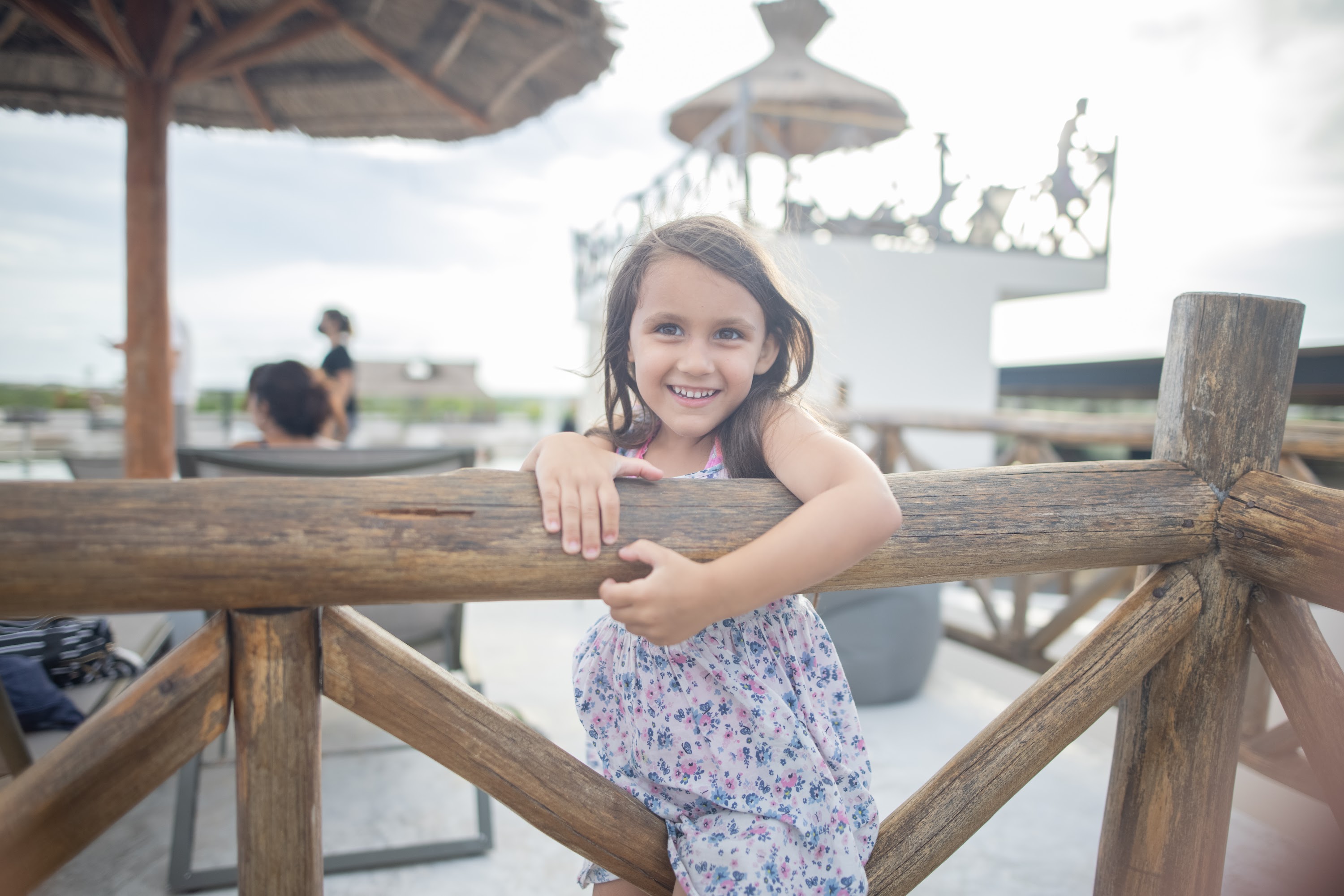 Smiling Girl Leaning on Wooden Railing at Outdoor Terrace