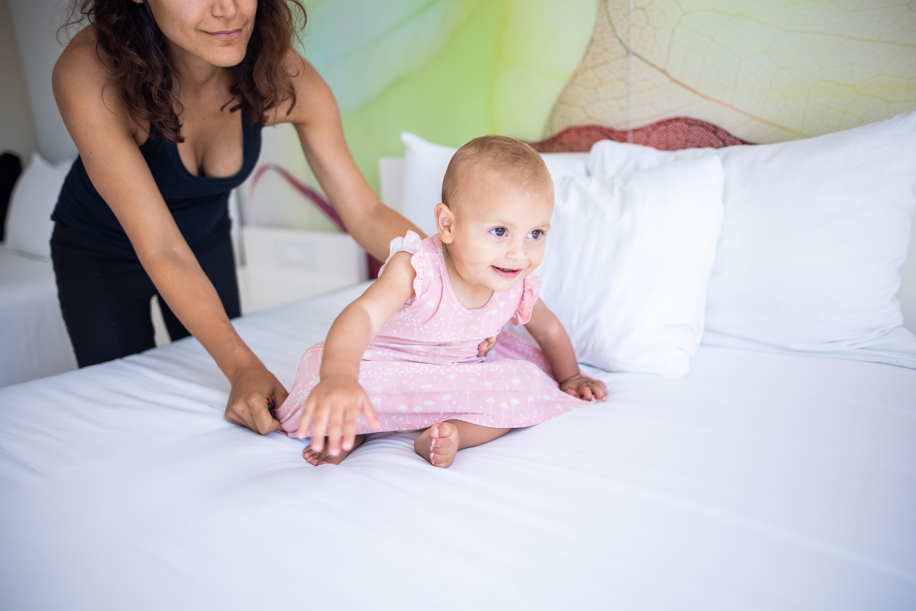 Mother helping baby sit on bed