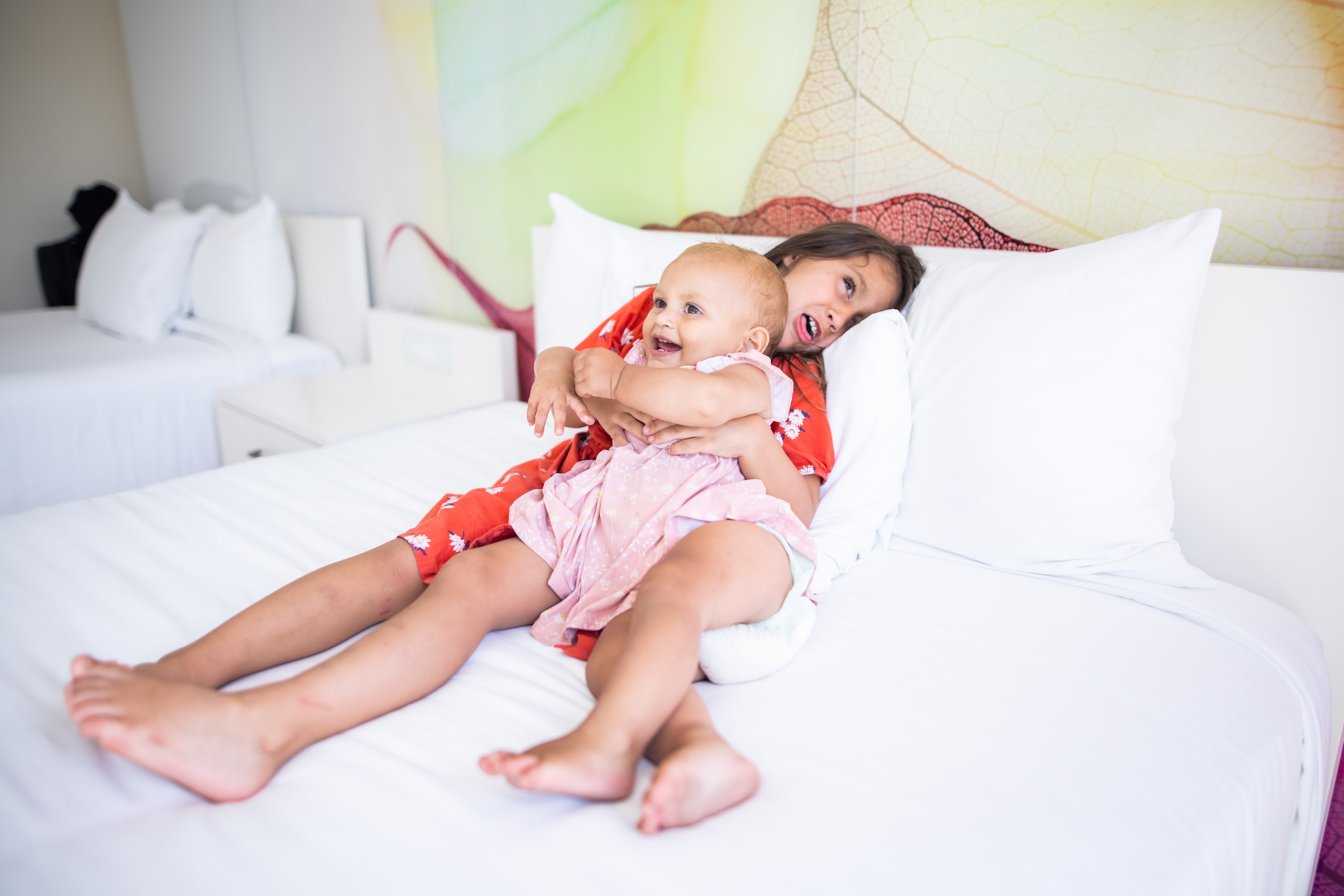 Sisters Embracing on a Bed in a Bright Hotel Room