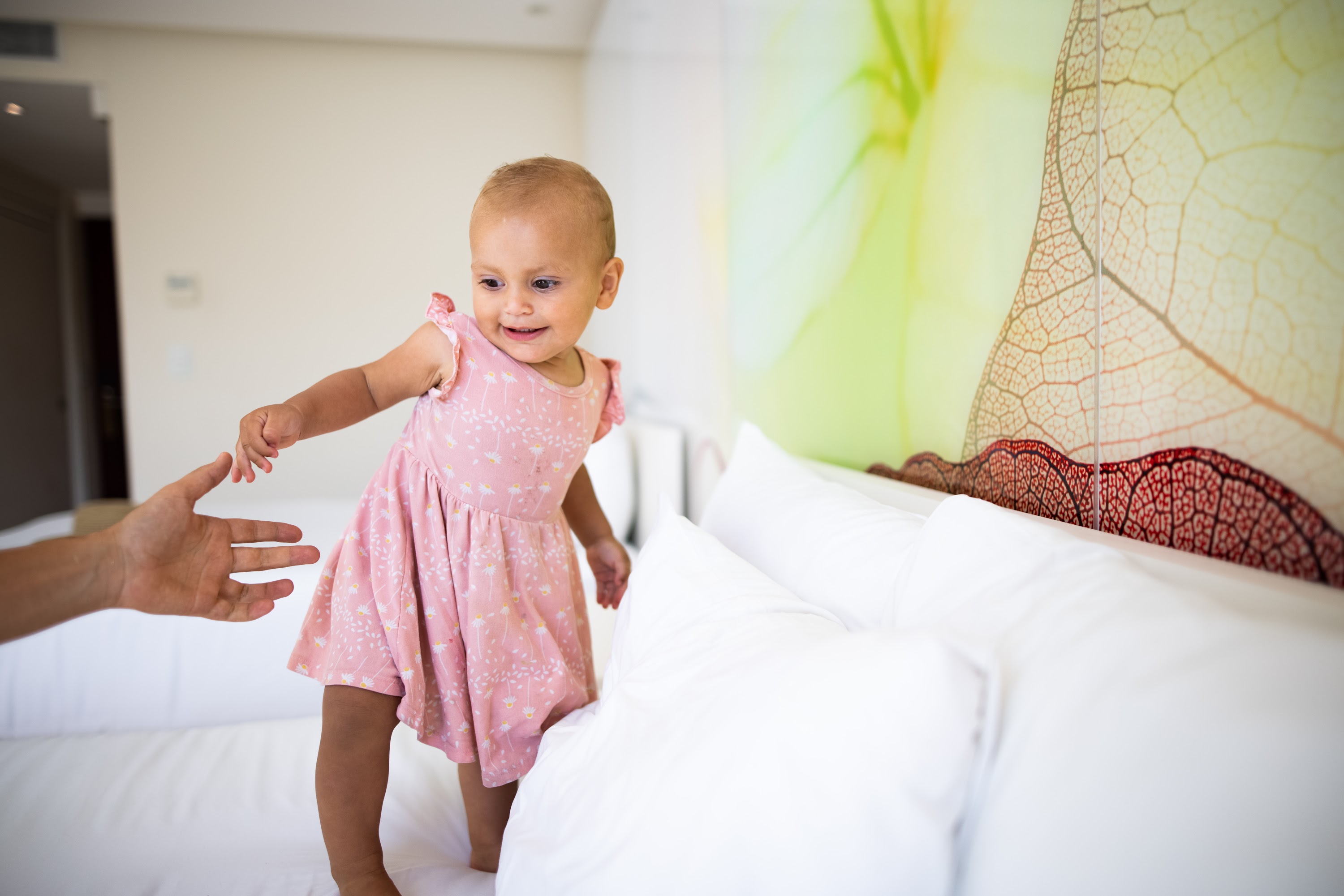 Baby Girl Stepping on Bed with Adult Hand Reaching Out