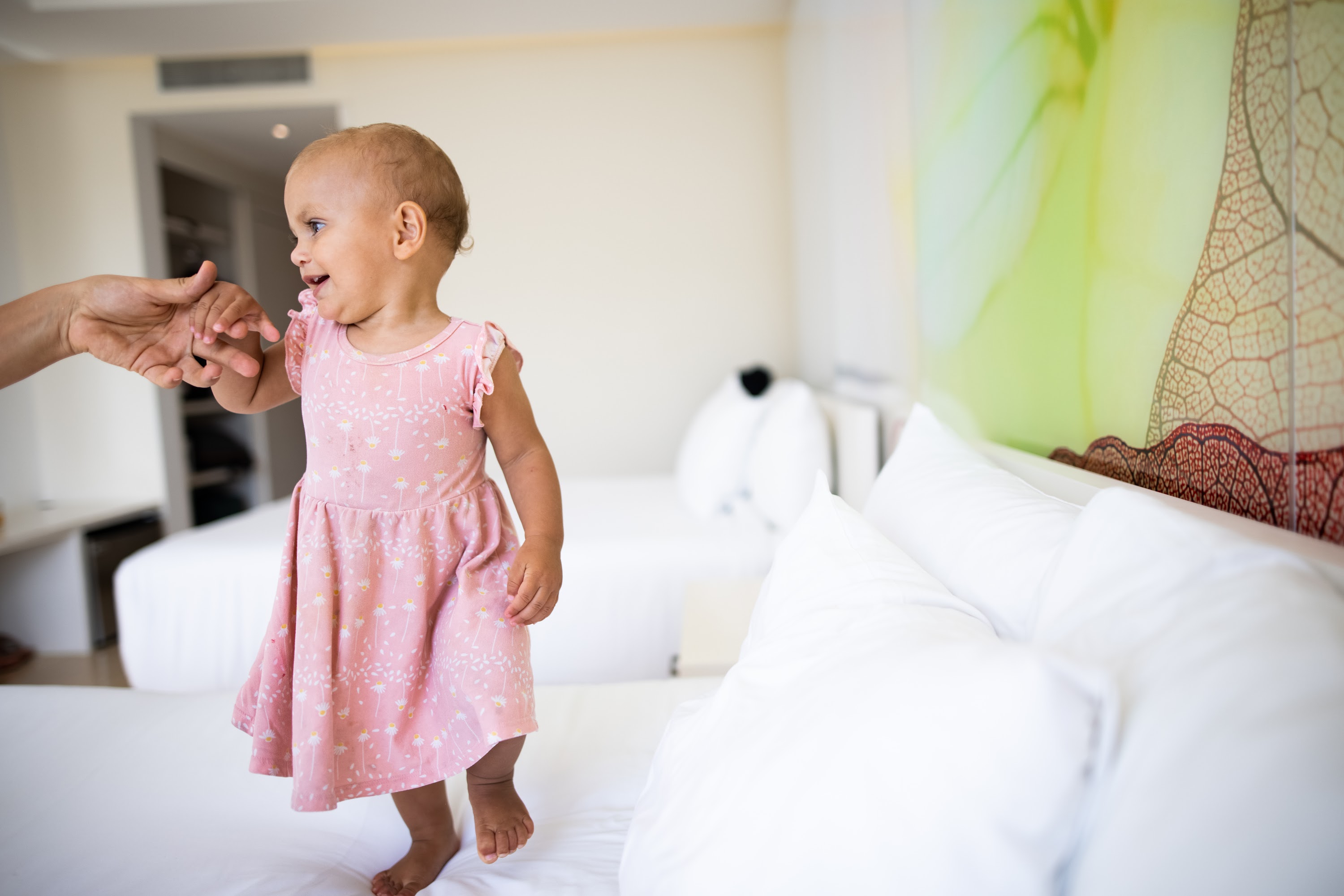 Baby in Pink Dress Holding Adult's Hand on Bed