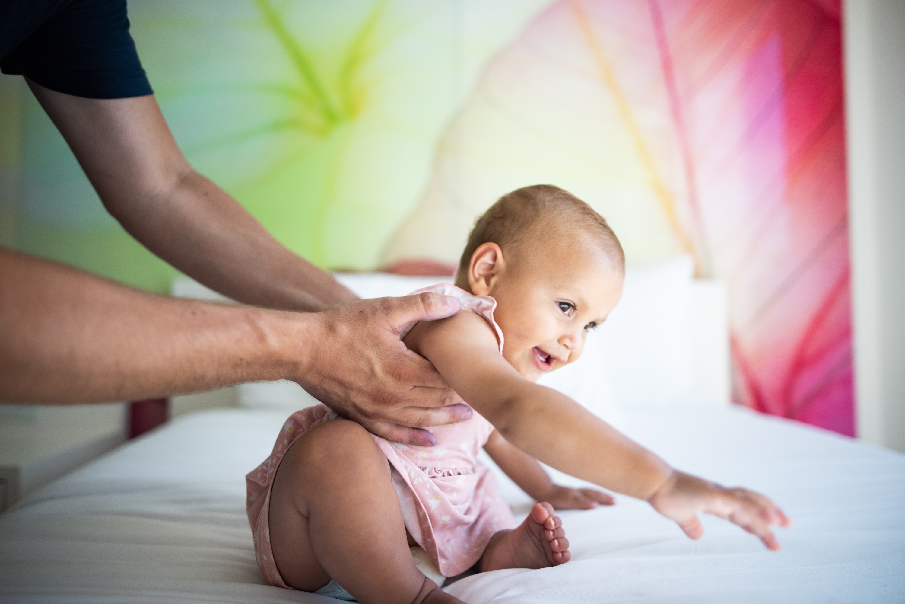 Baby Playing on Bed with Adult Hands Supporting
