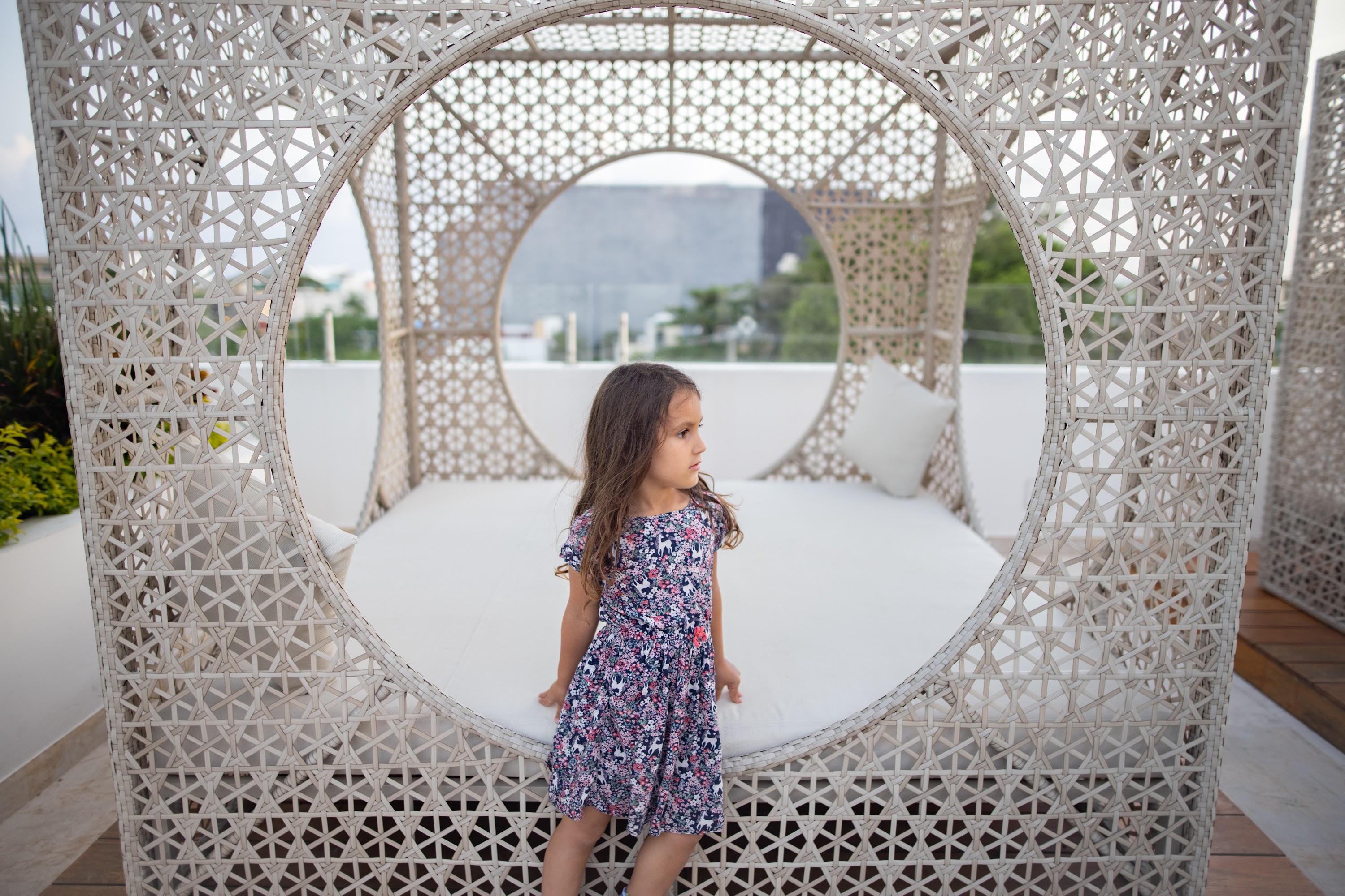 Girl in Floral Dress Standing by Woven Outdoor Lounger