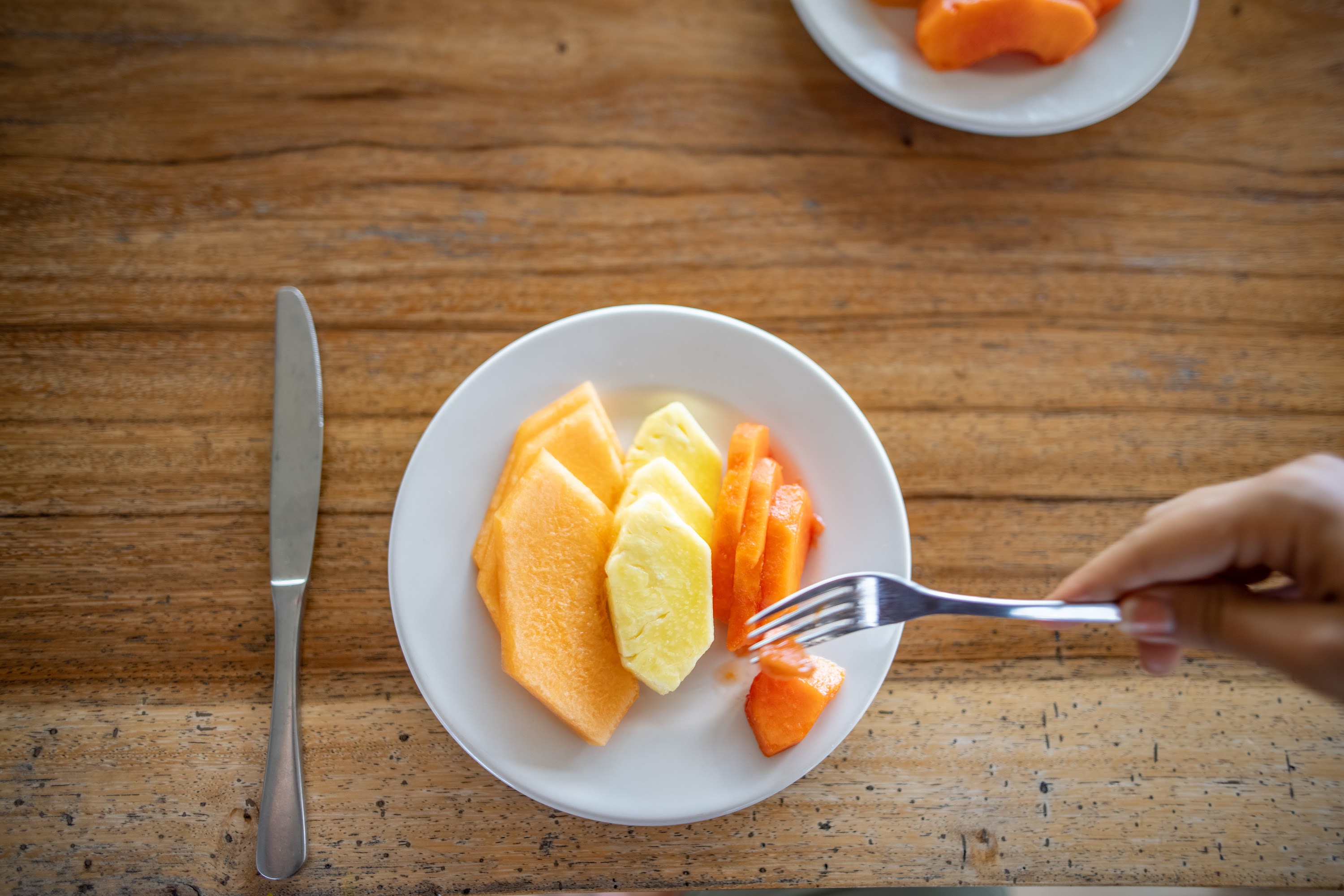 Hand Picking Fruit from a Plate on Wooden Table