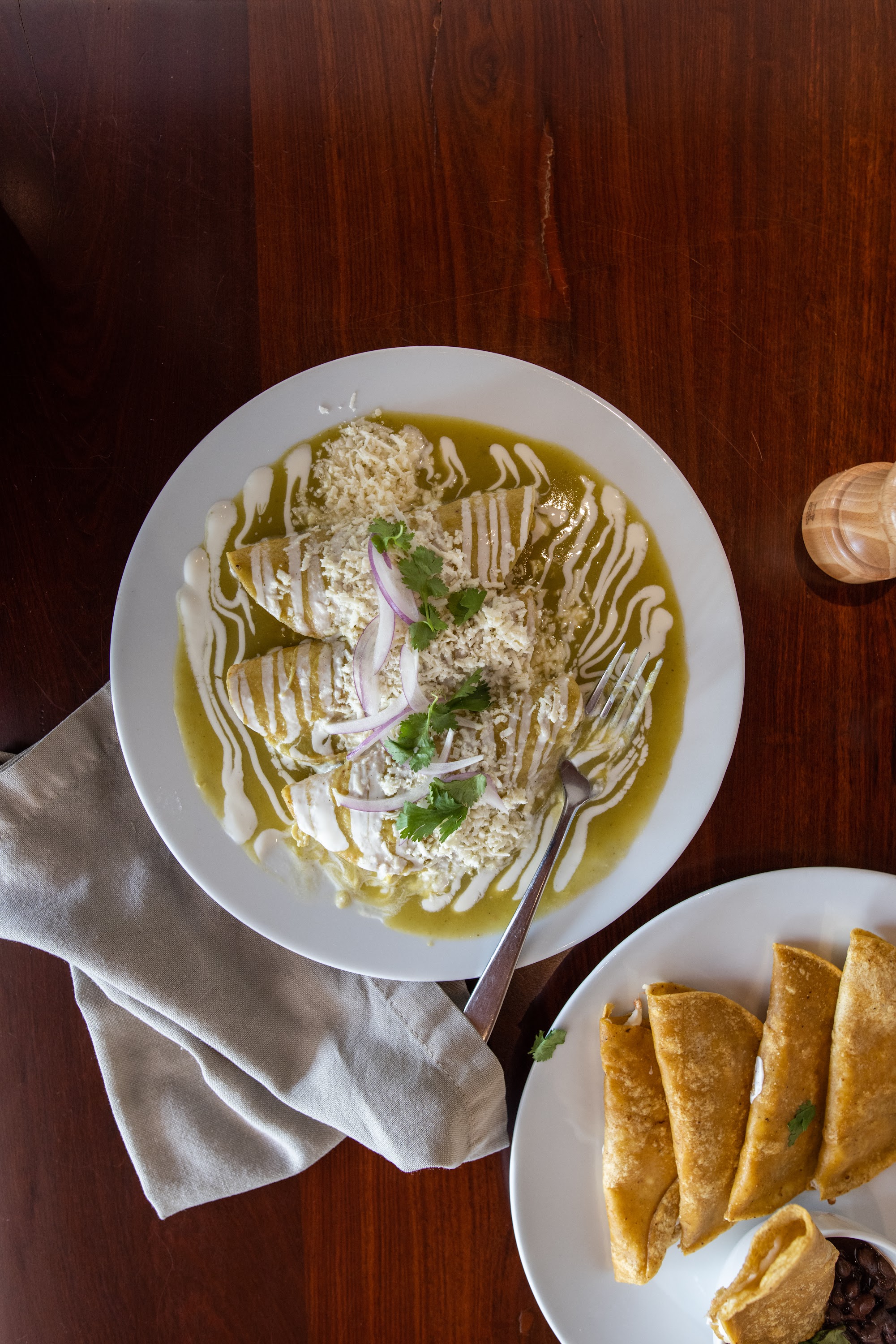 Top-down view of green chile enchiladas and taquitos on a wooden table