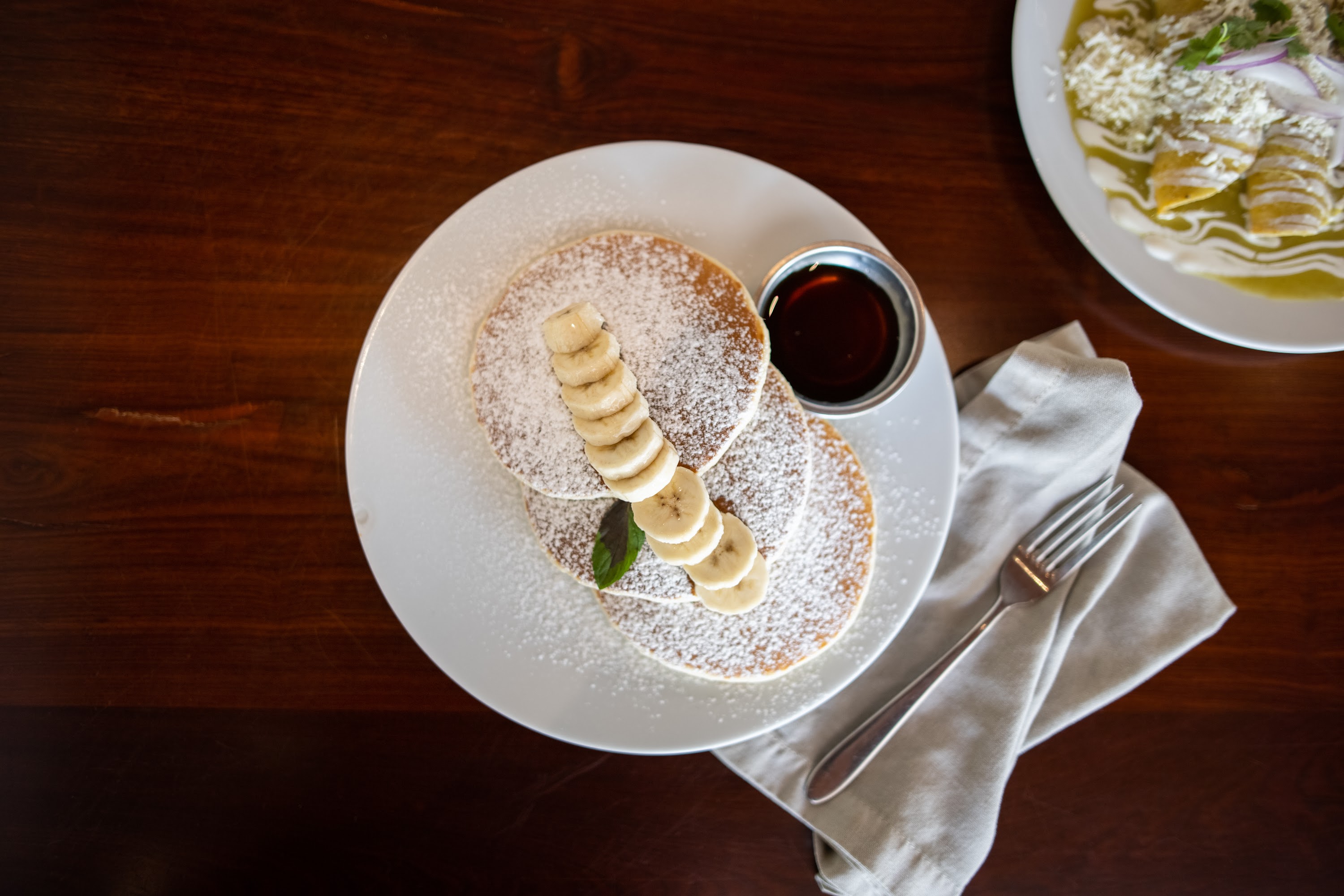 Overhead view of banana pancakes with syrup and powdered sugar
