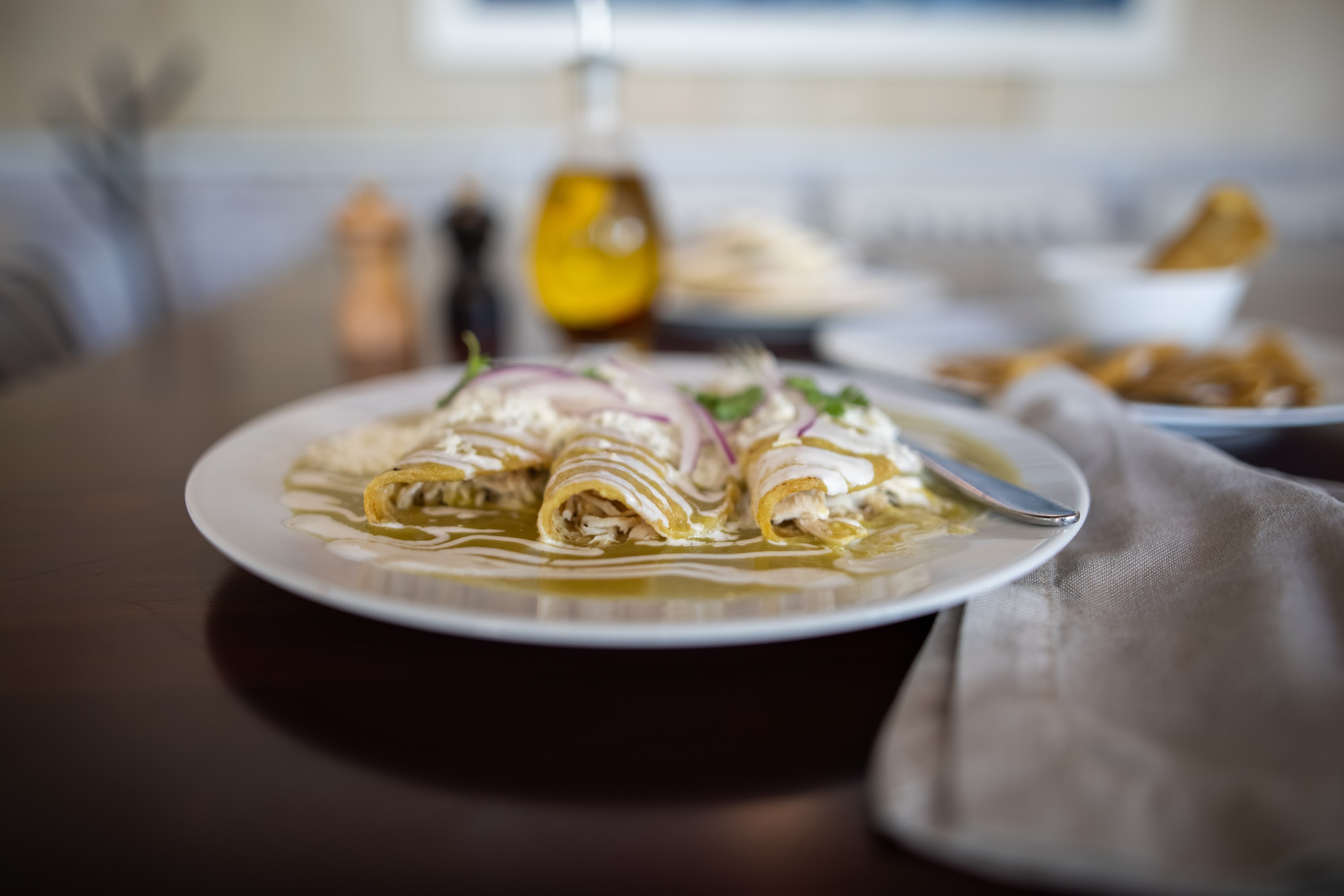 Enchiladas Verdes with Crema and Red Onion on White Plate