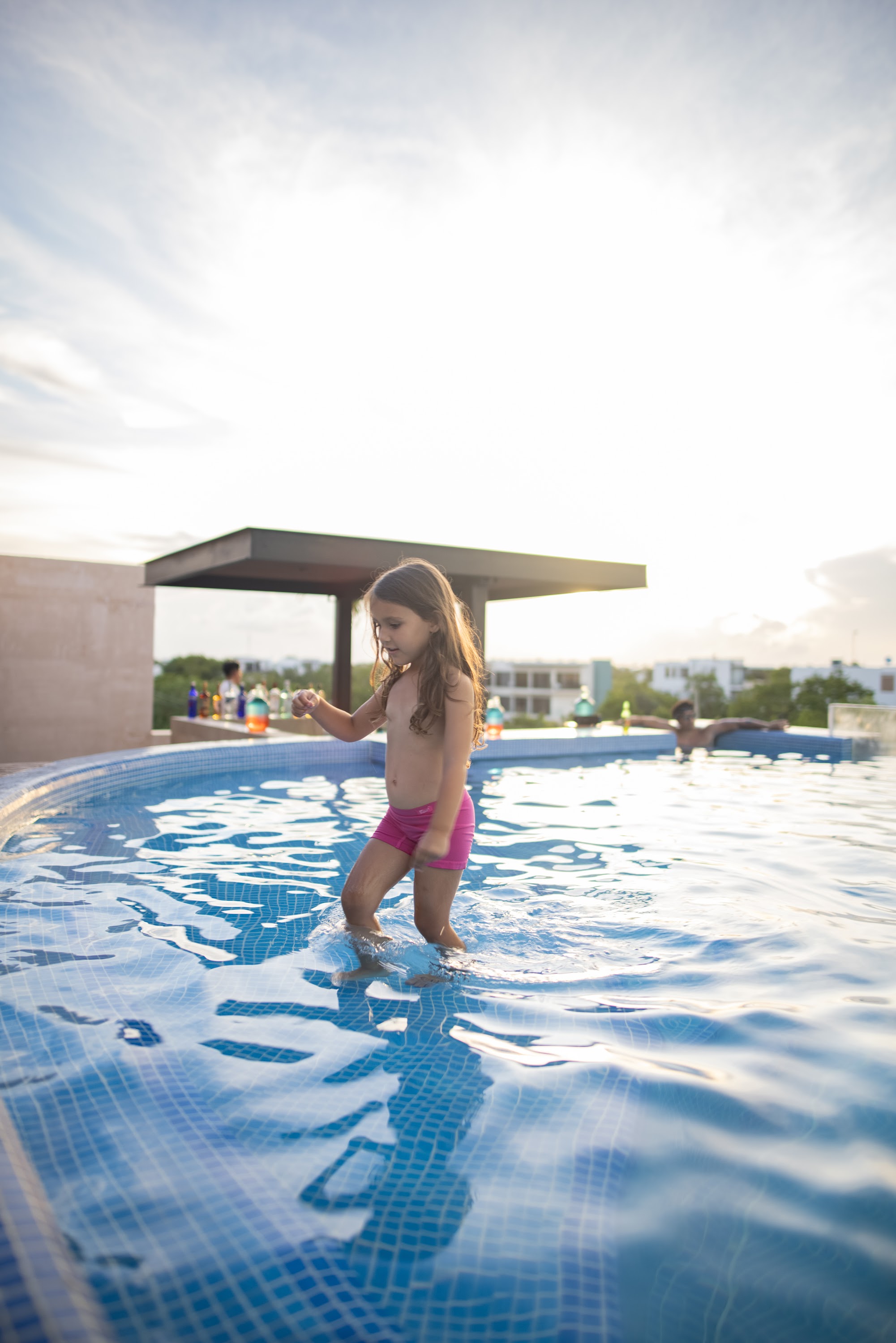 Young Girl in Pink Swimwear Walking in Pool at Sunset