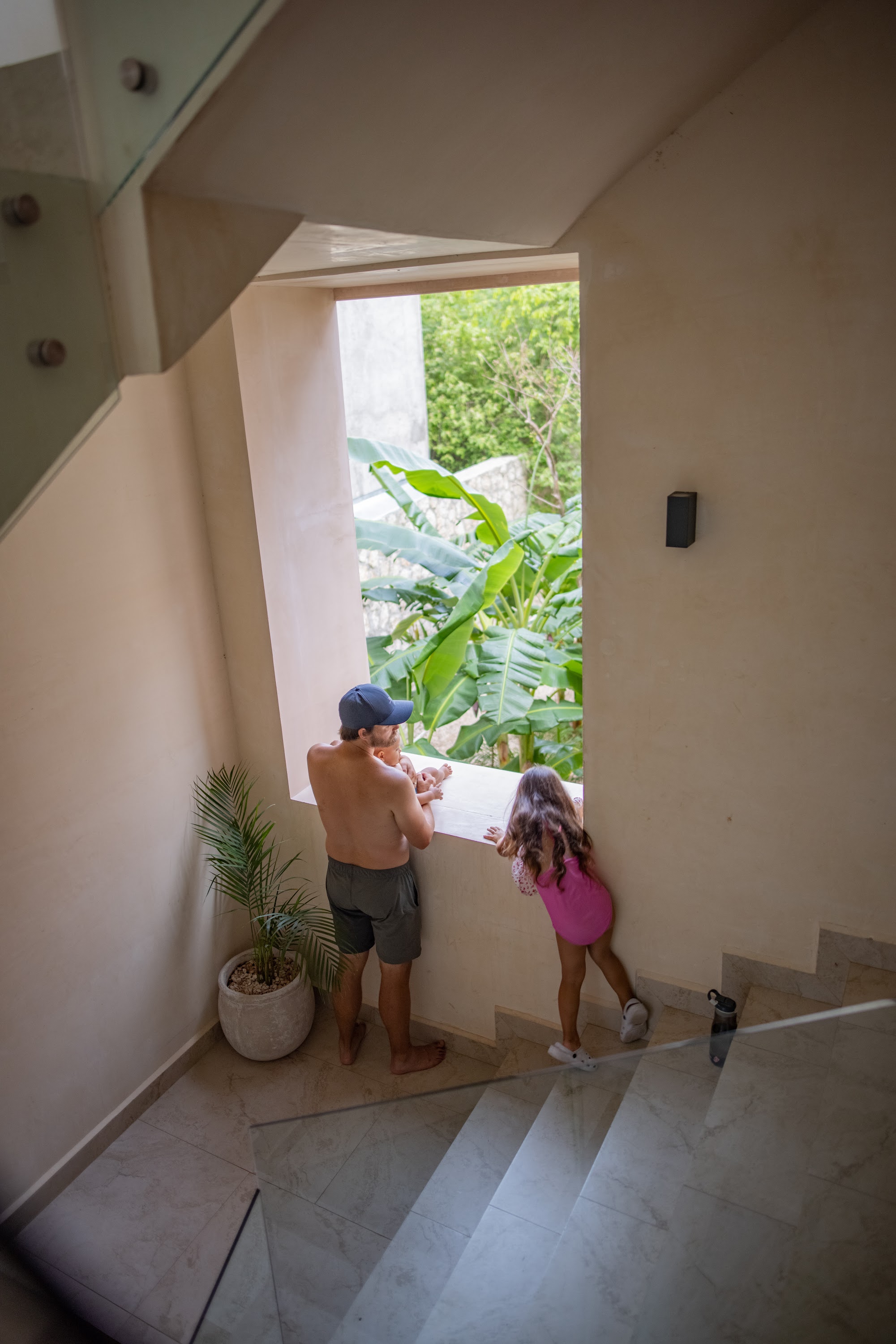 Father and Daughter Gazing Out a Window at Tropical Plants