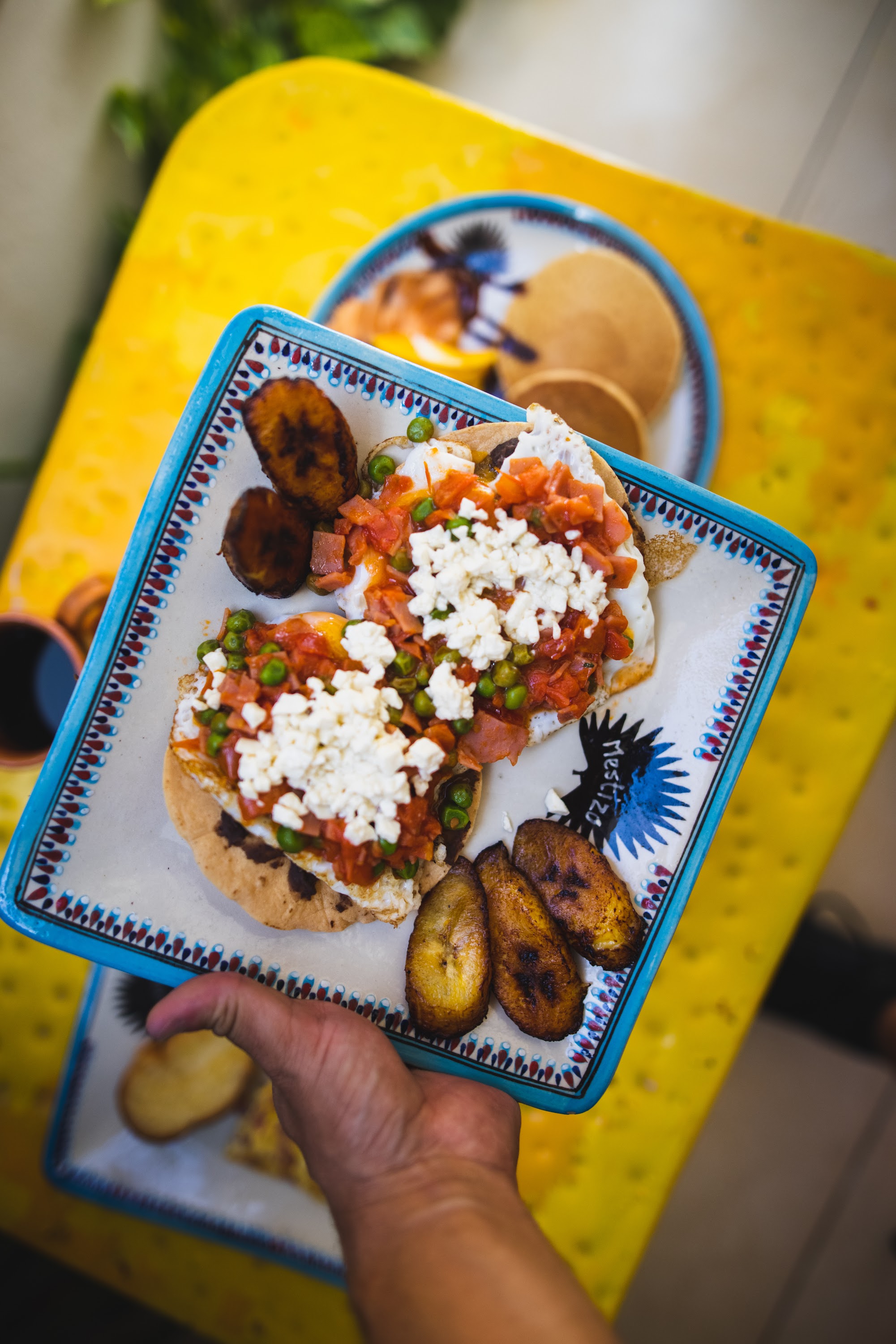 Hand Holding Plate of Breakfast Tostadas with Plantains