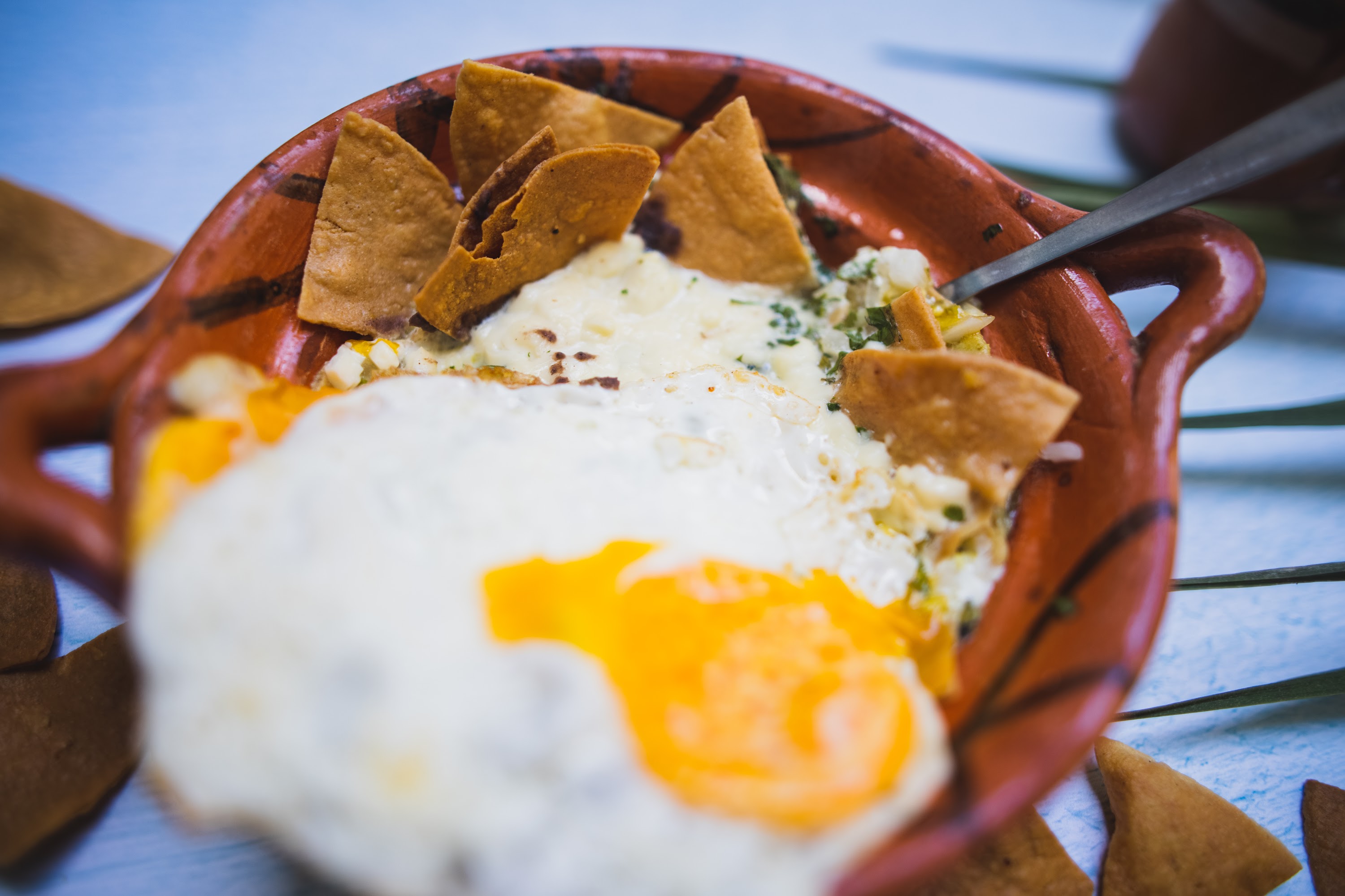 Mexican-style dish with fried egg and tortilla chips in clay bowl