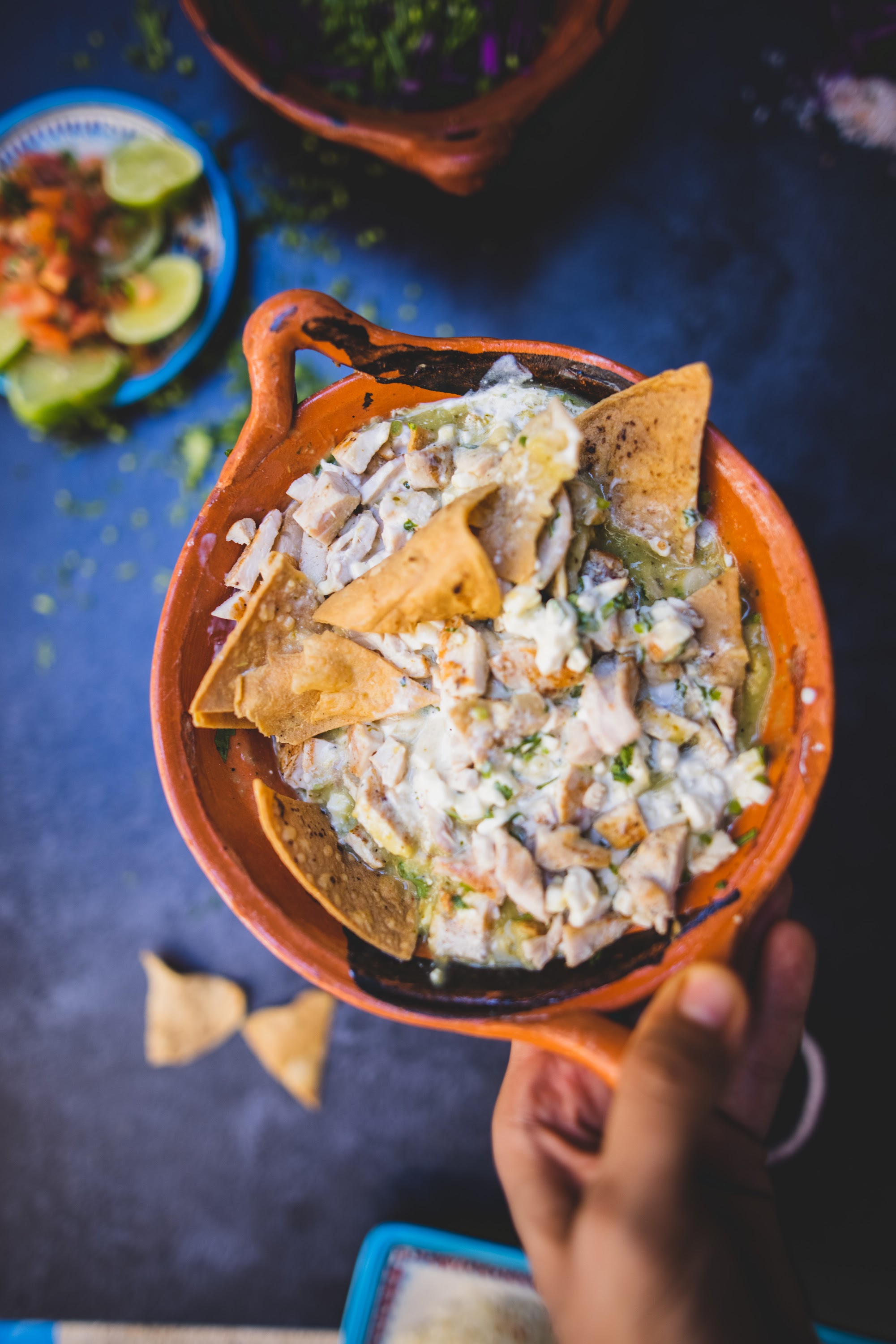 Hand Holding Clay Bowl of Mexican Fish Soup with Tortilla Chips