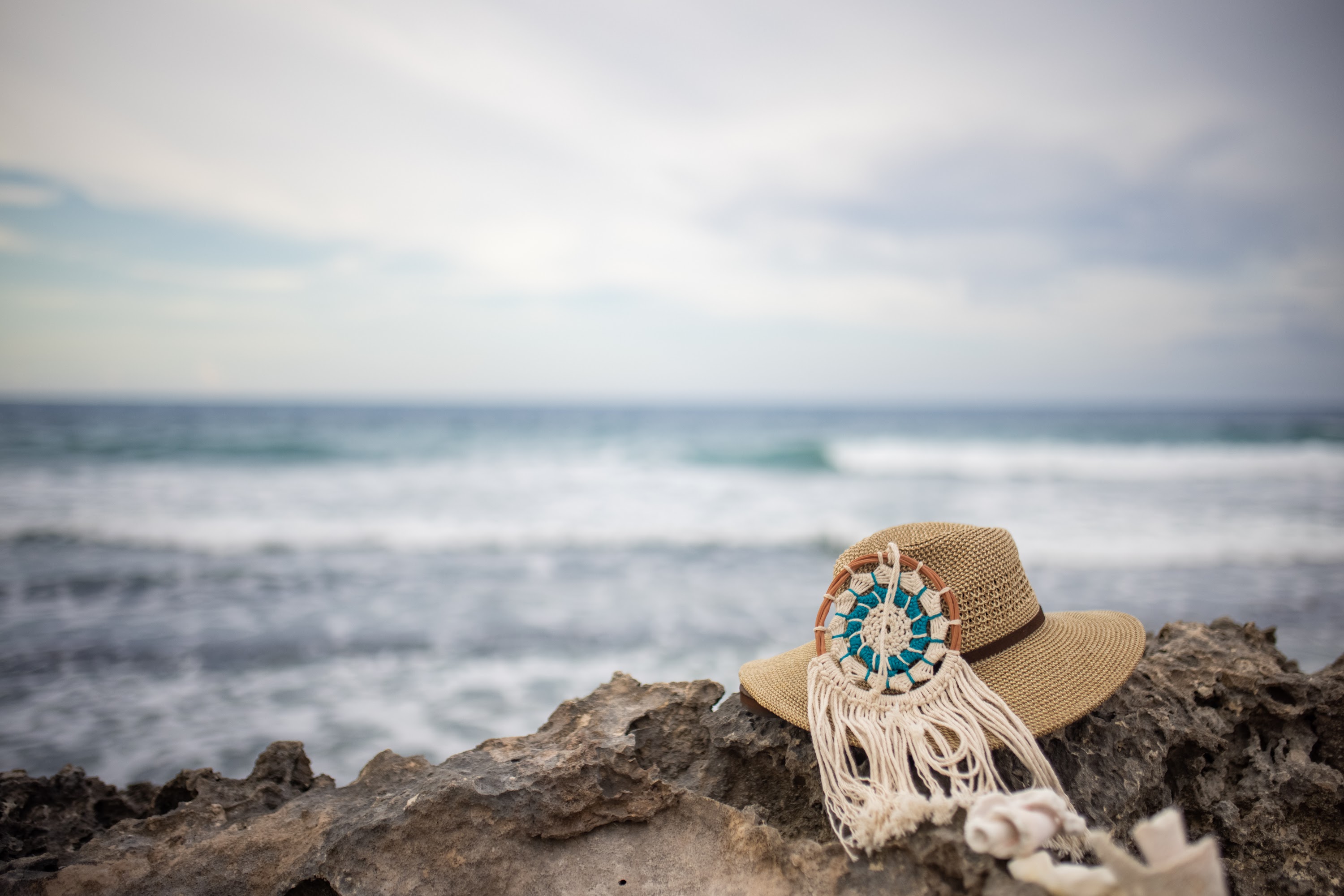 Straw Hat with Macrame Ornament on Ocean Rocks