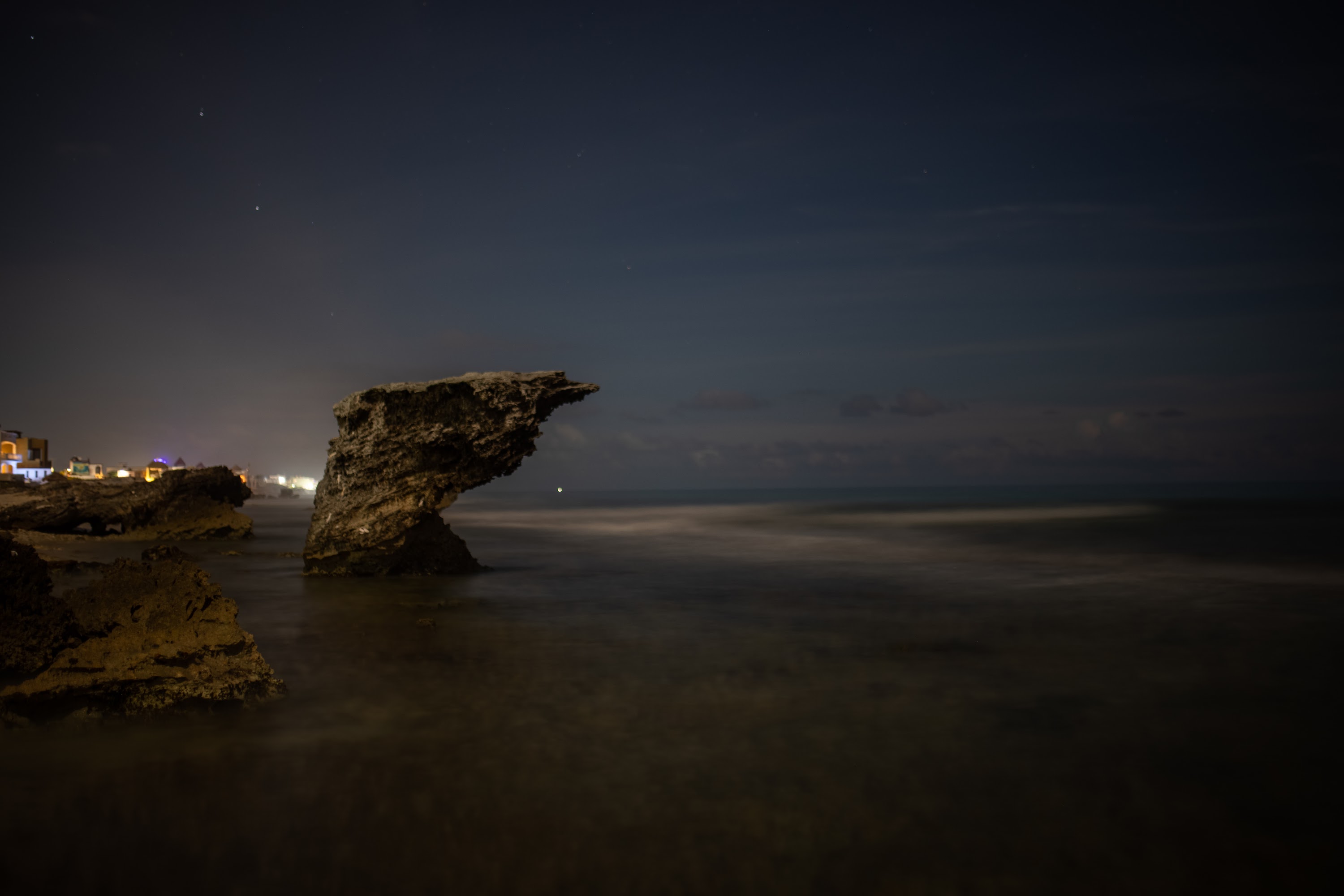 Nighttime Coastal Rock Formation with City Lights