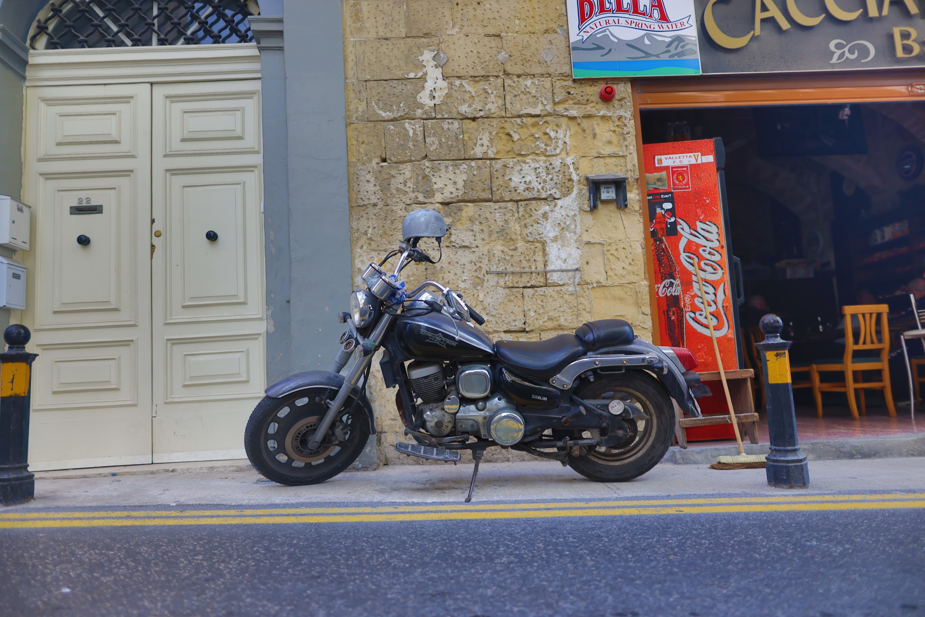 Black motorcycle parked on street beside vintage Coca-Cola machine