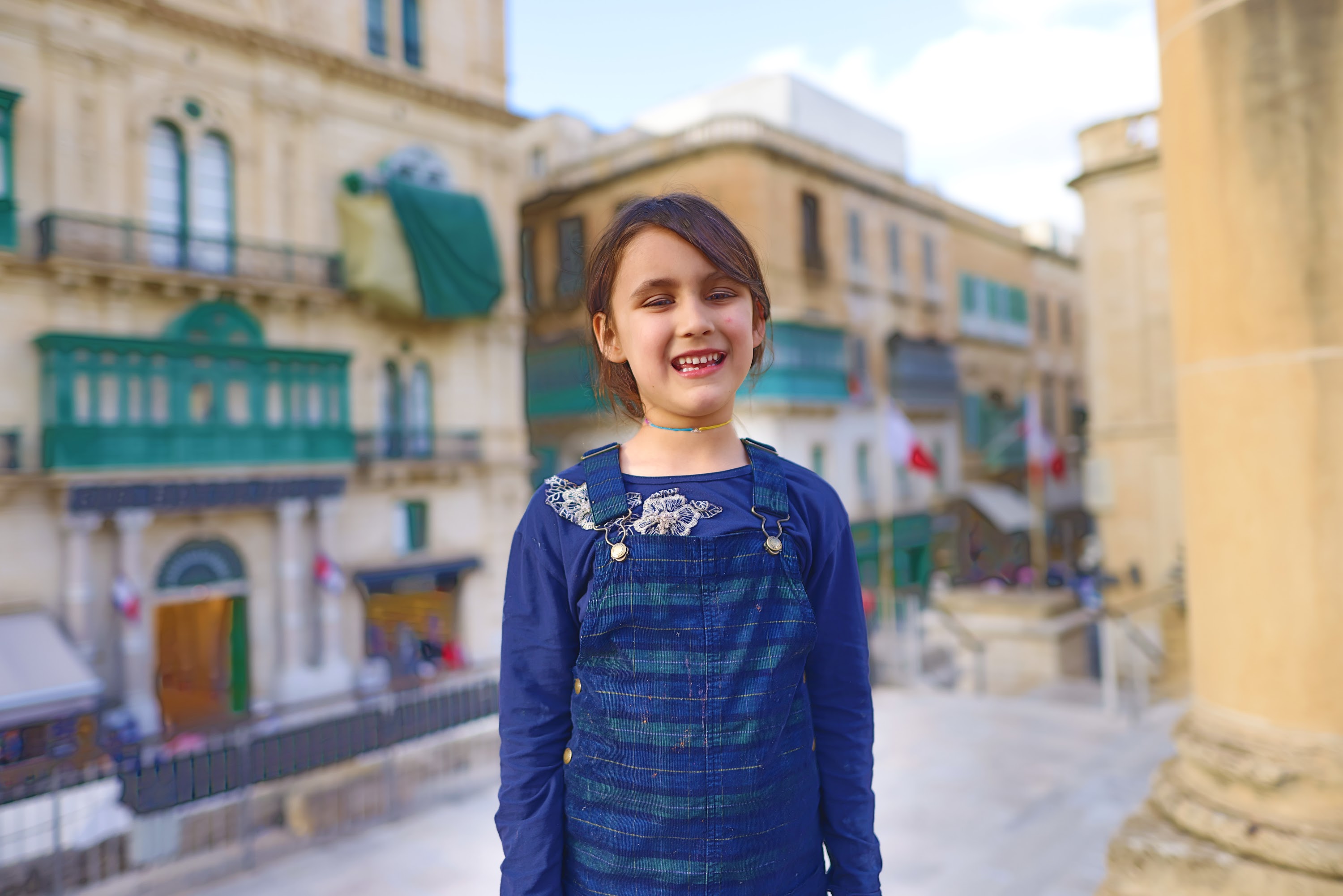 Smiling Girl in Overalls on a Historic Street