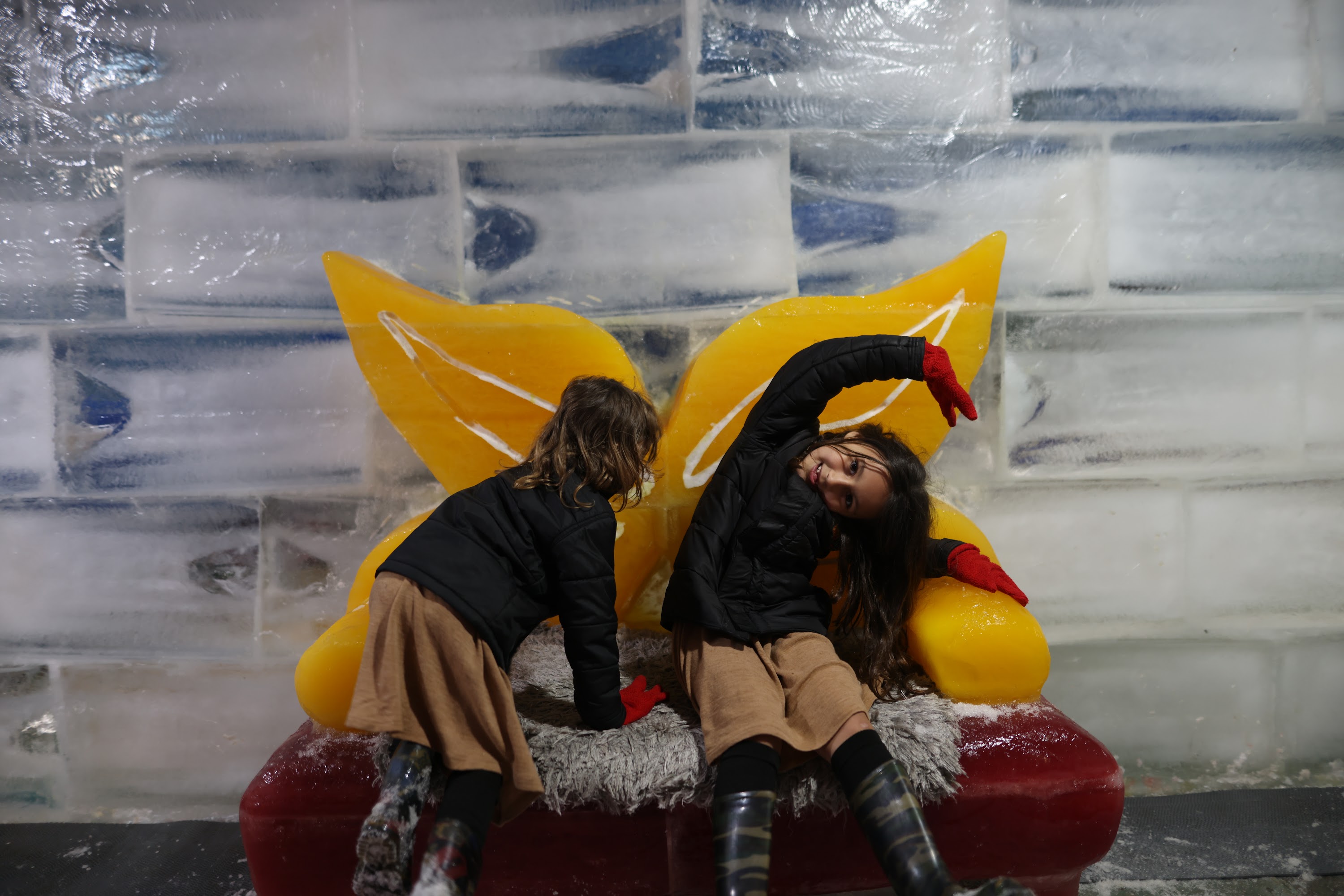 Two Girls Playing on Ice Sculpture with Yellow Wings
