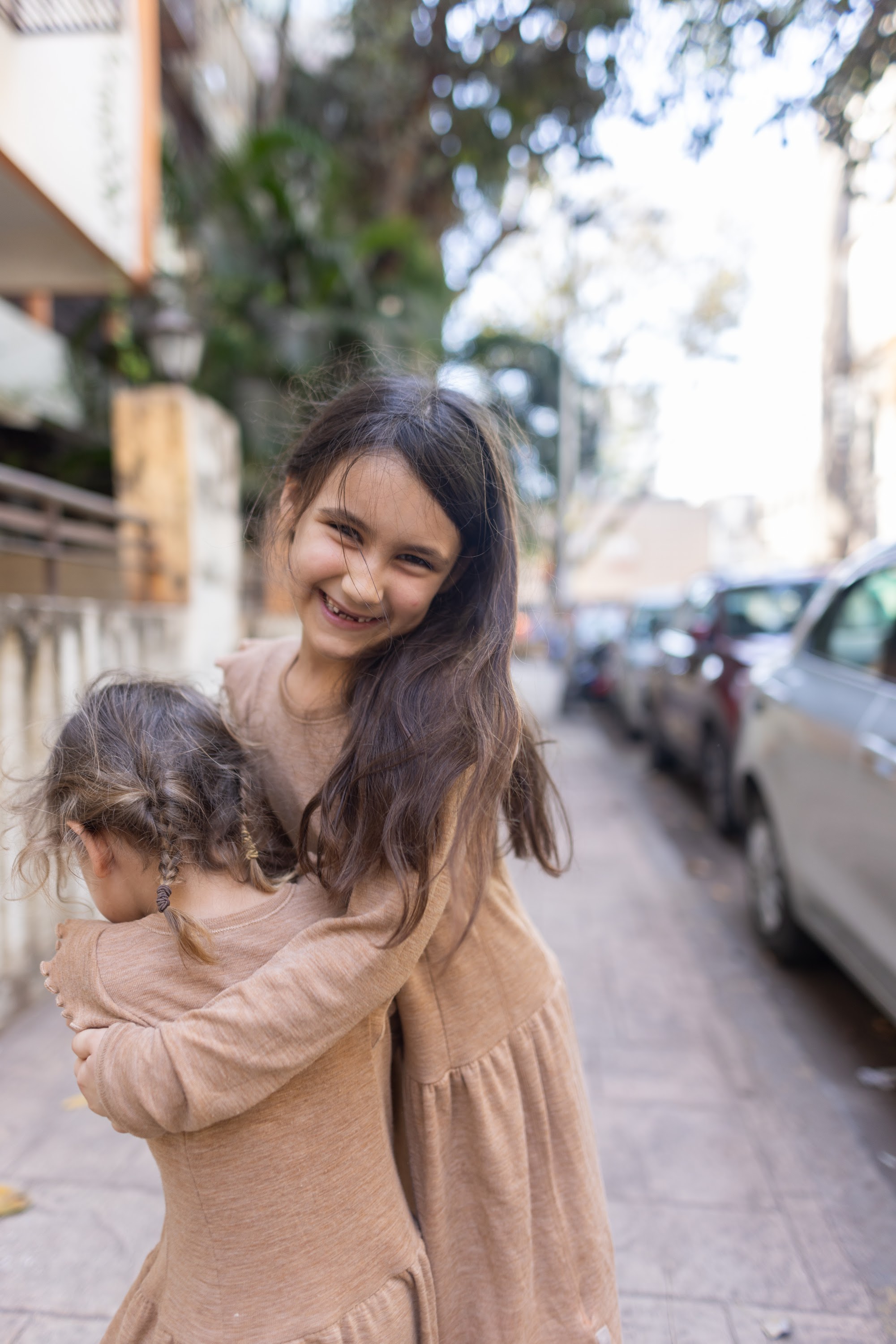 Two Girls Hugging on a City Sidewalk