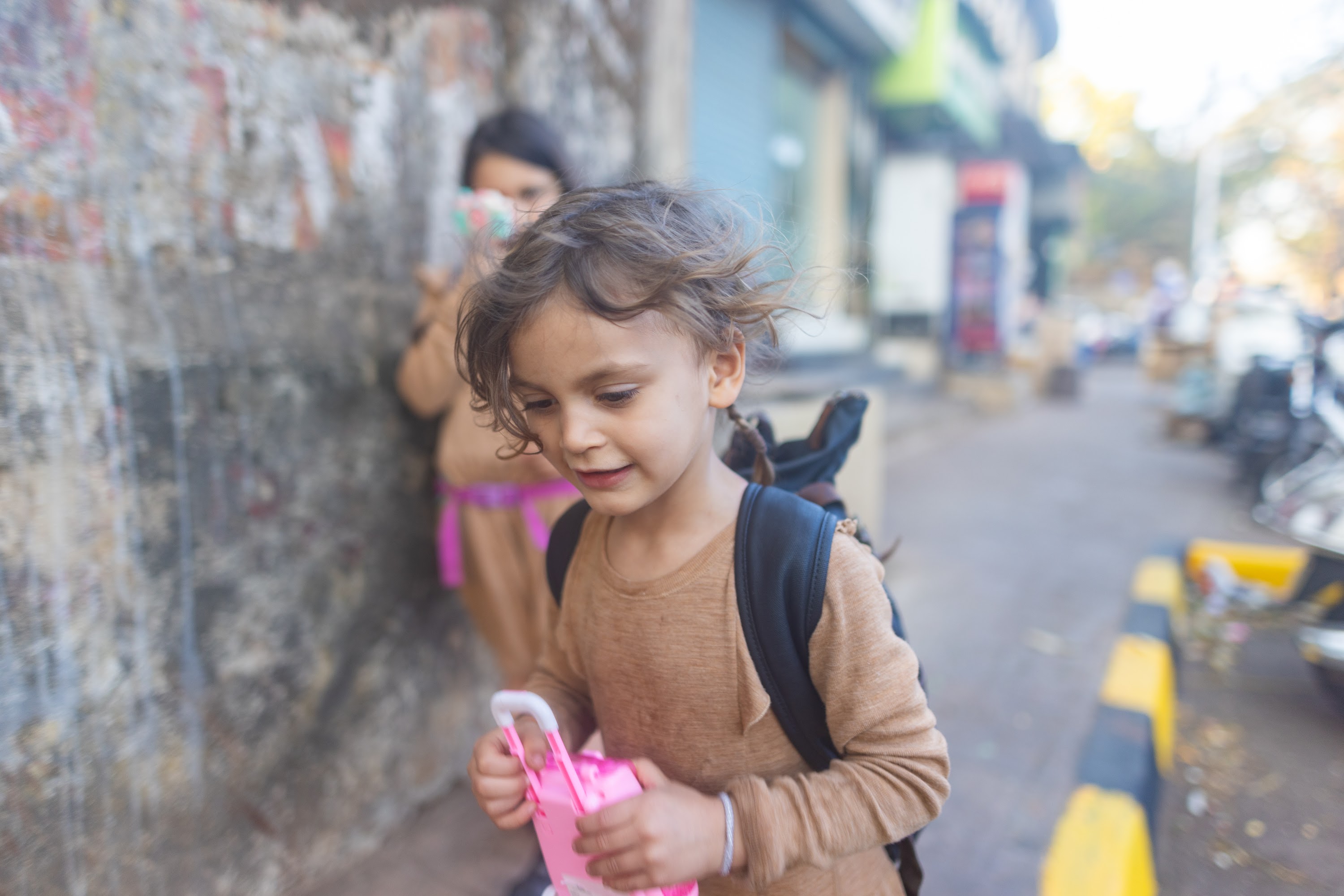 Child Holding Pink Toy on Street
