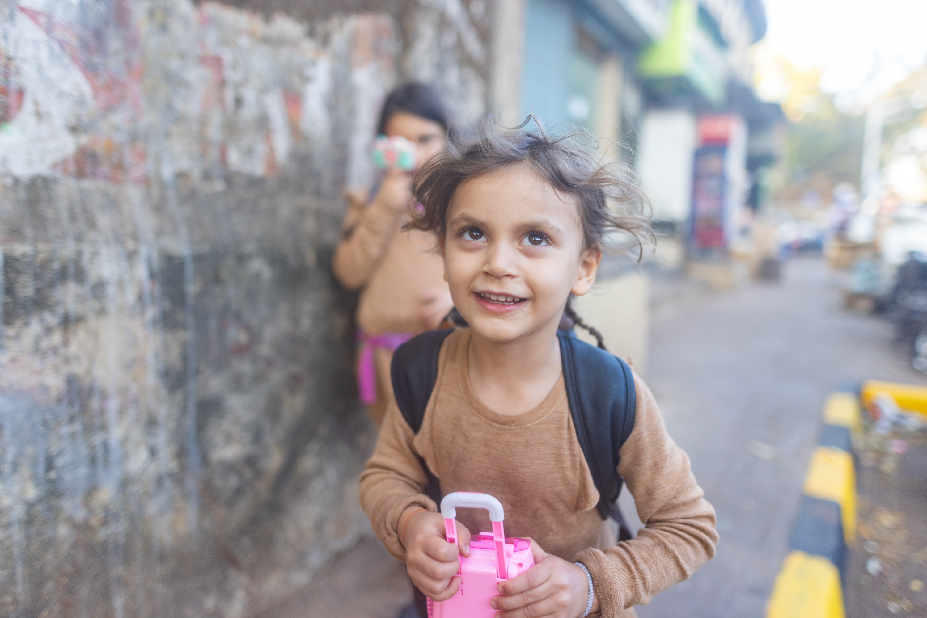 Smiling Girl Holding Pink Toy Suitcase on Street
