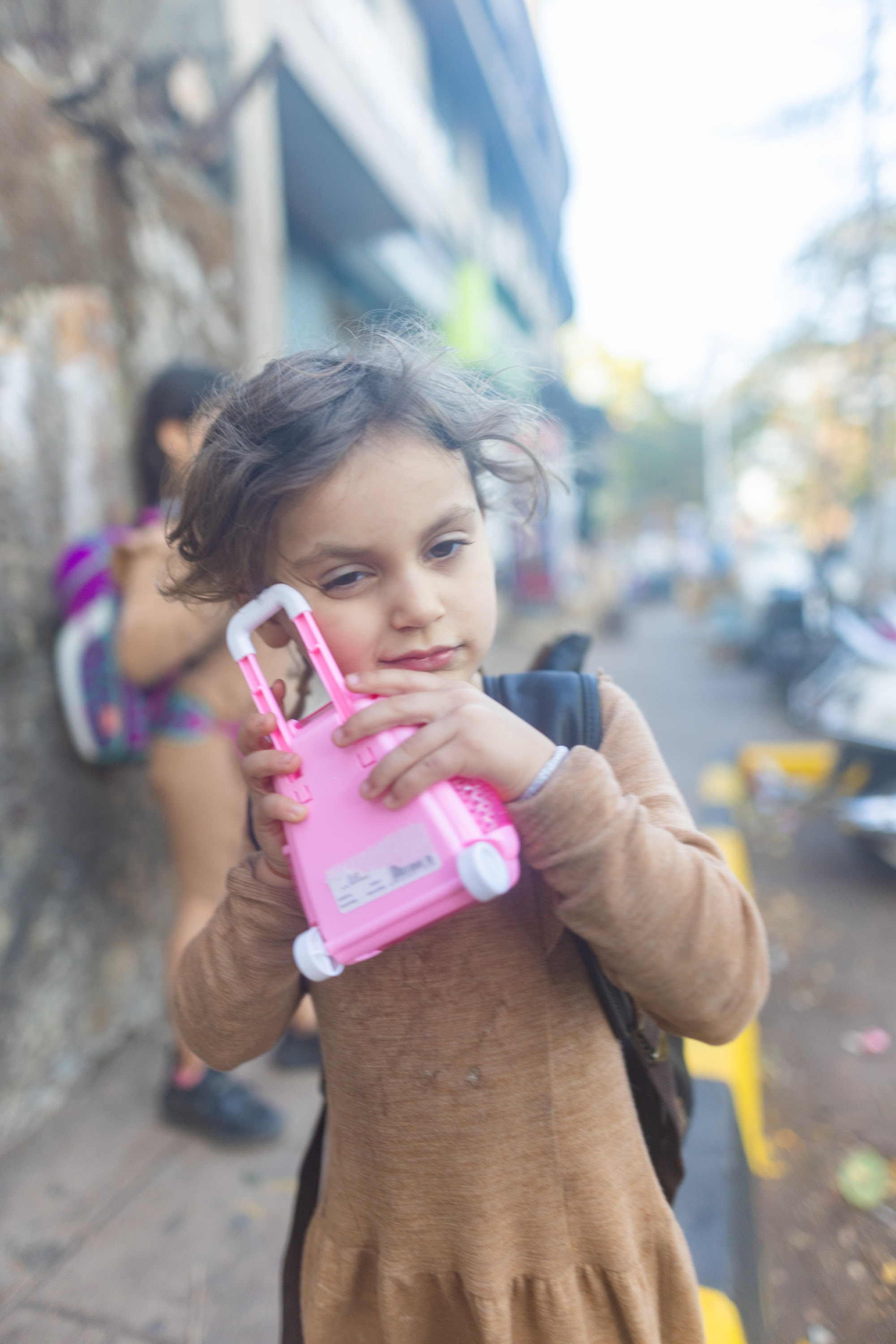 Child Holding Pink Toy Suitcase on Street
