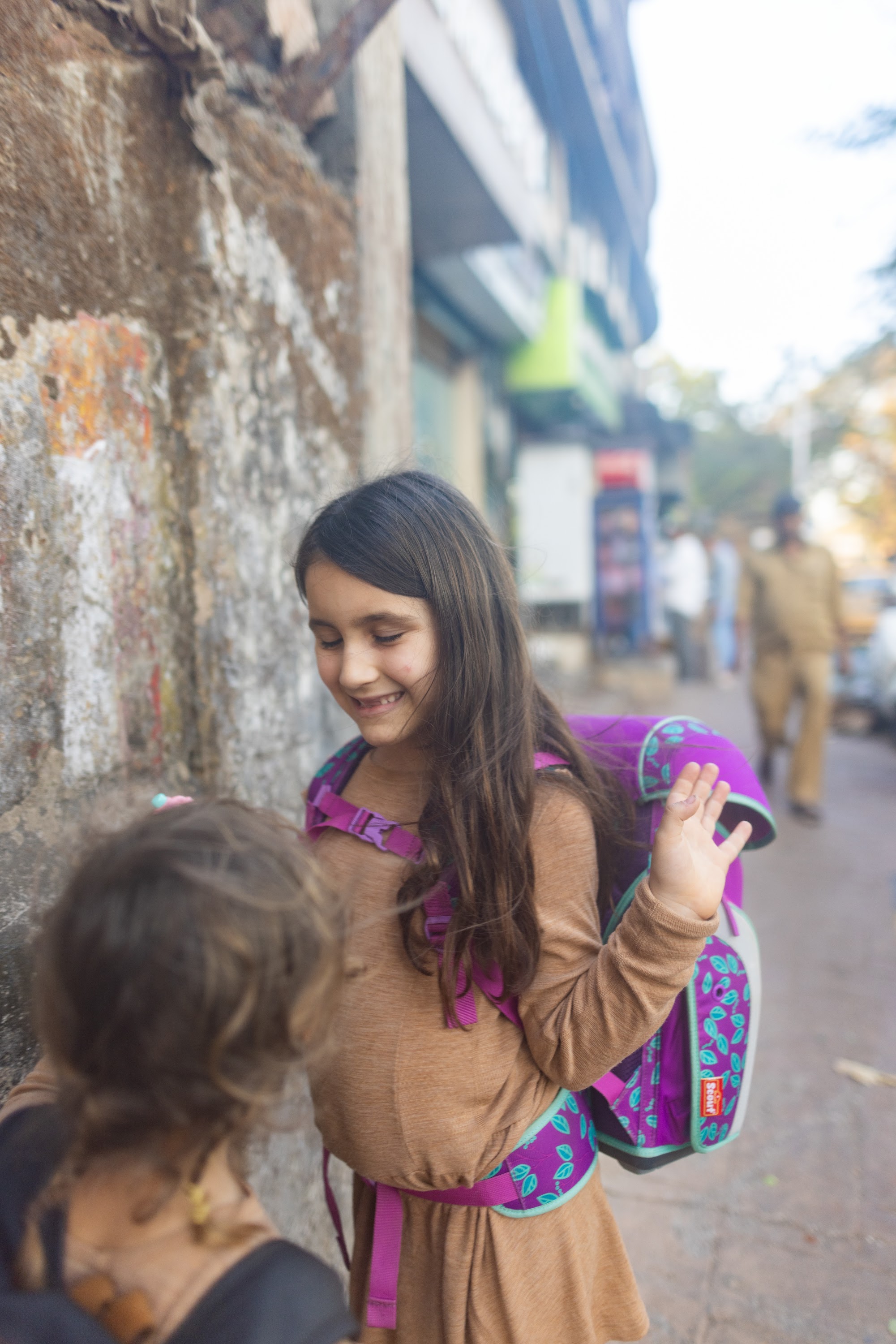 Girl Waving on Street with Backpack