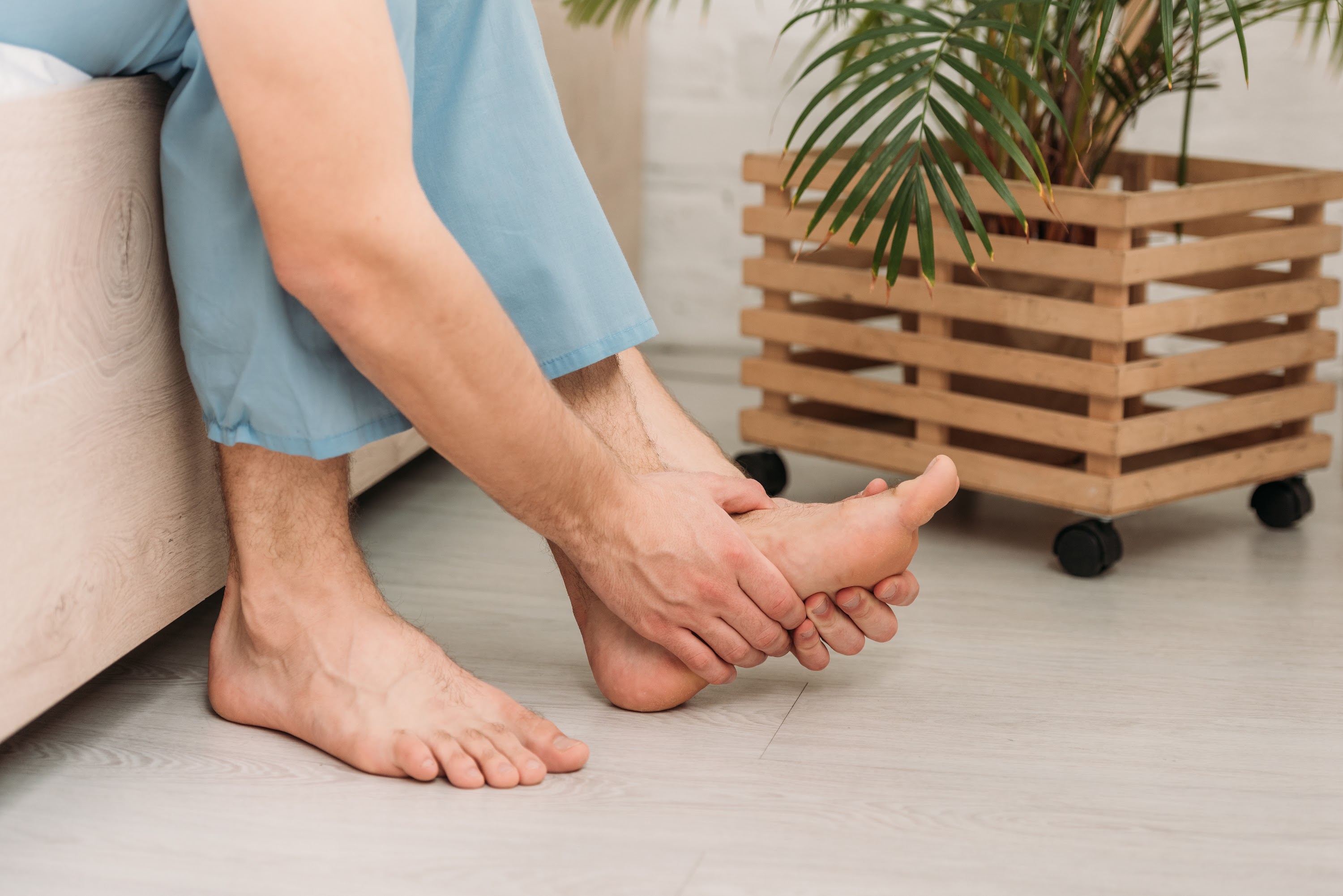 cropped-view-man-touching-foot-while-sitting-on-be-2023-11-27-05-23-25-utc.jpg