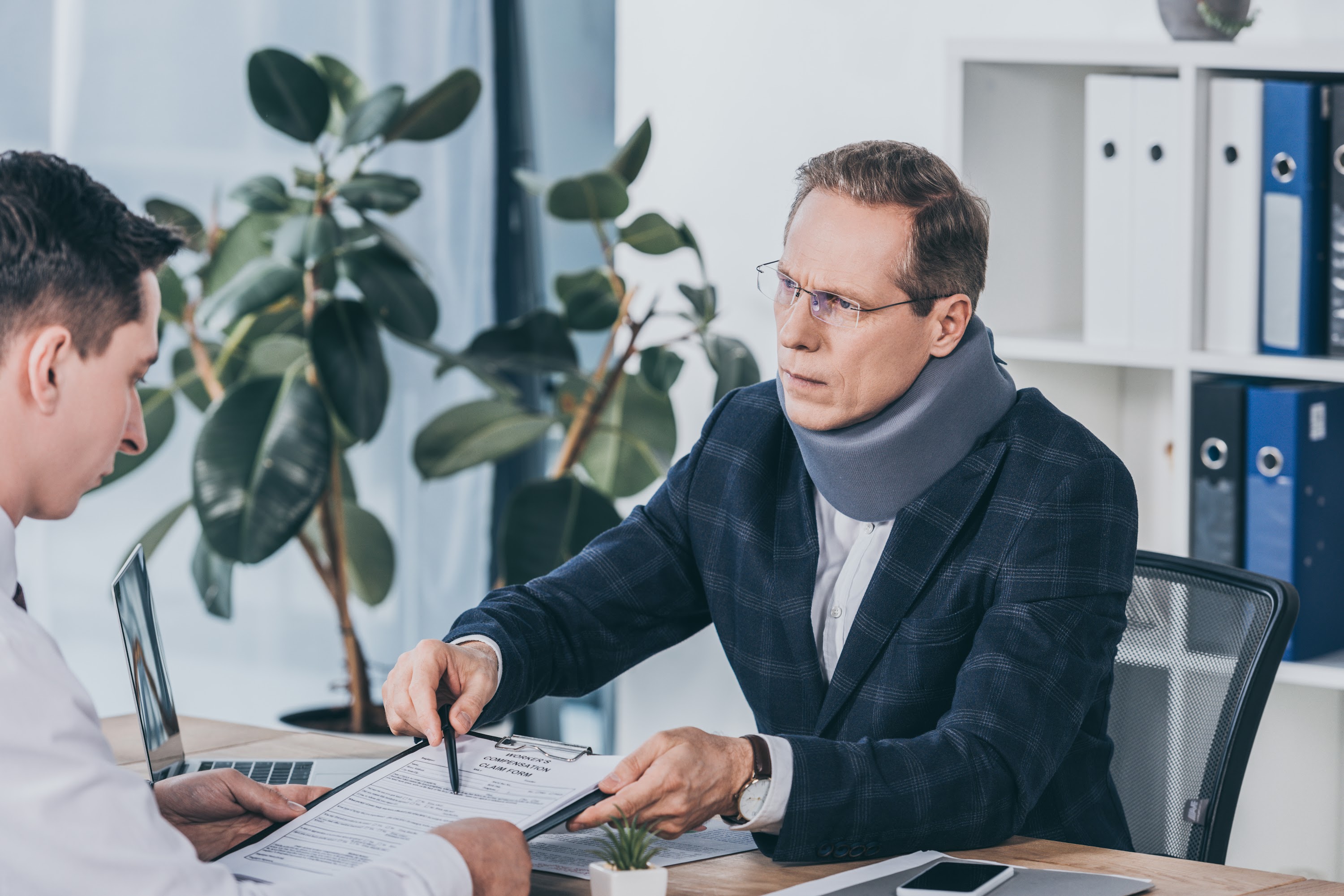 businessman-in-neck-brace-sitting-at-table-and-poi-2023-11-27-05-01-36-utc (1).jpg