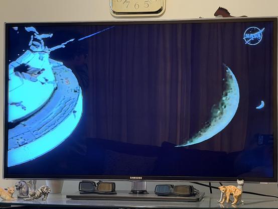 TV showing view from the Artemis solar array. The spacecraft is on the left. A crescent moon (far side) is towards the right, and a tiny crescent Earth is on the right.