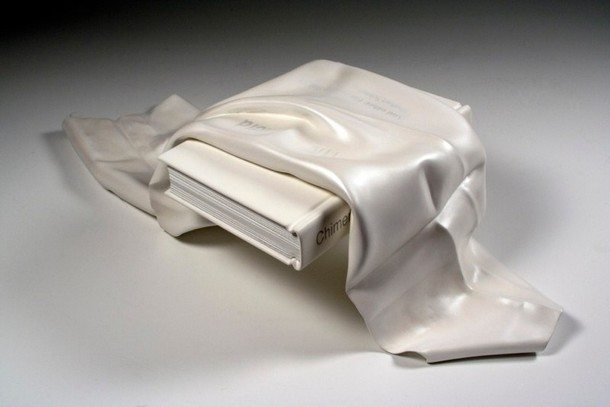 A piece of white fabric lying ove a book, both carved on wood